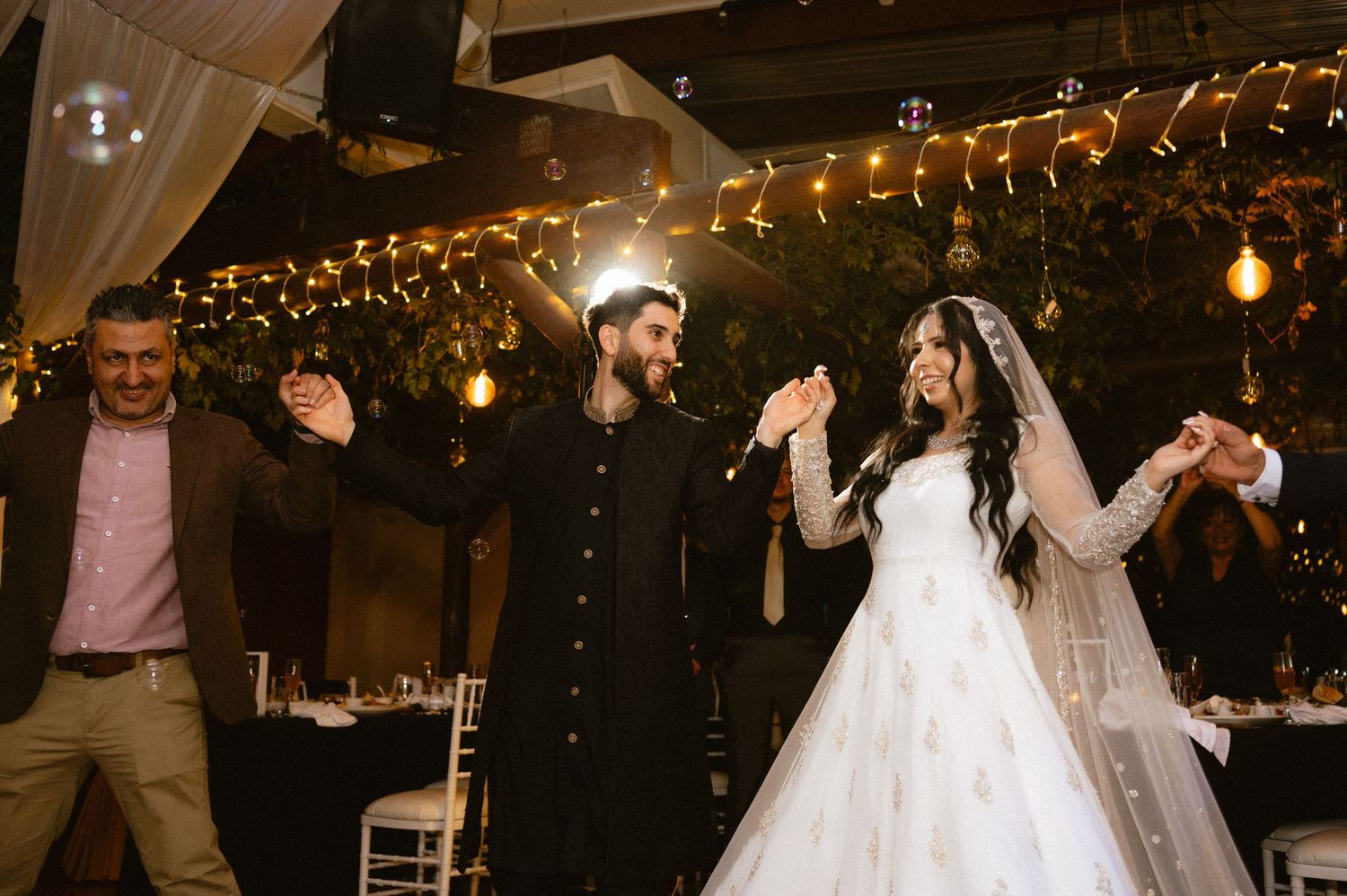 Wedding reception celebration with string lights creating a warm ambiance in a dark venue.
