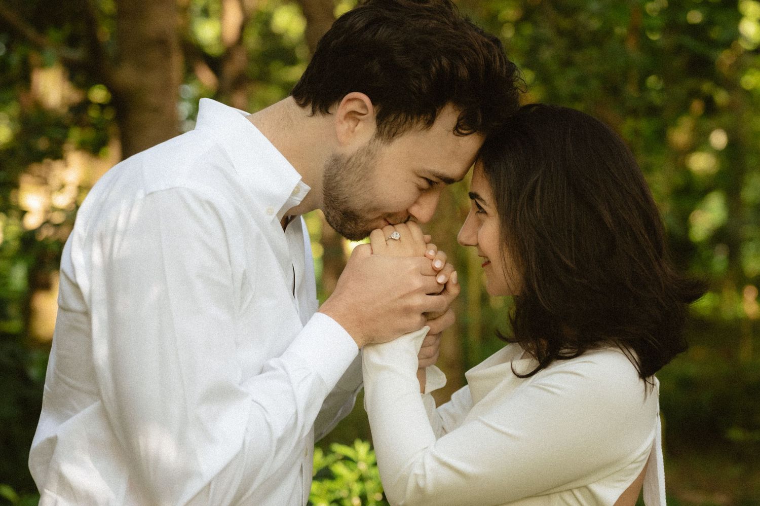 Engagement Photoshoot in the forest with guy and girl holding hands touching forehead and staring at each other.