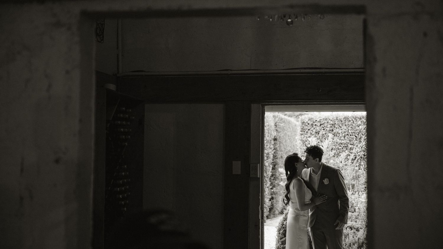 Black and white photo of a couple sharing a romantic kiss in a doorway on their wedding day.