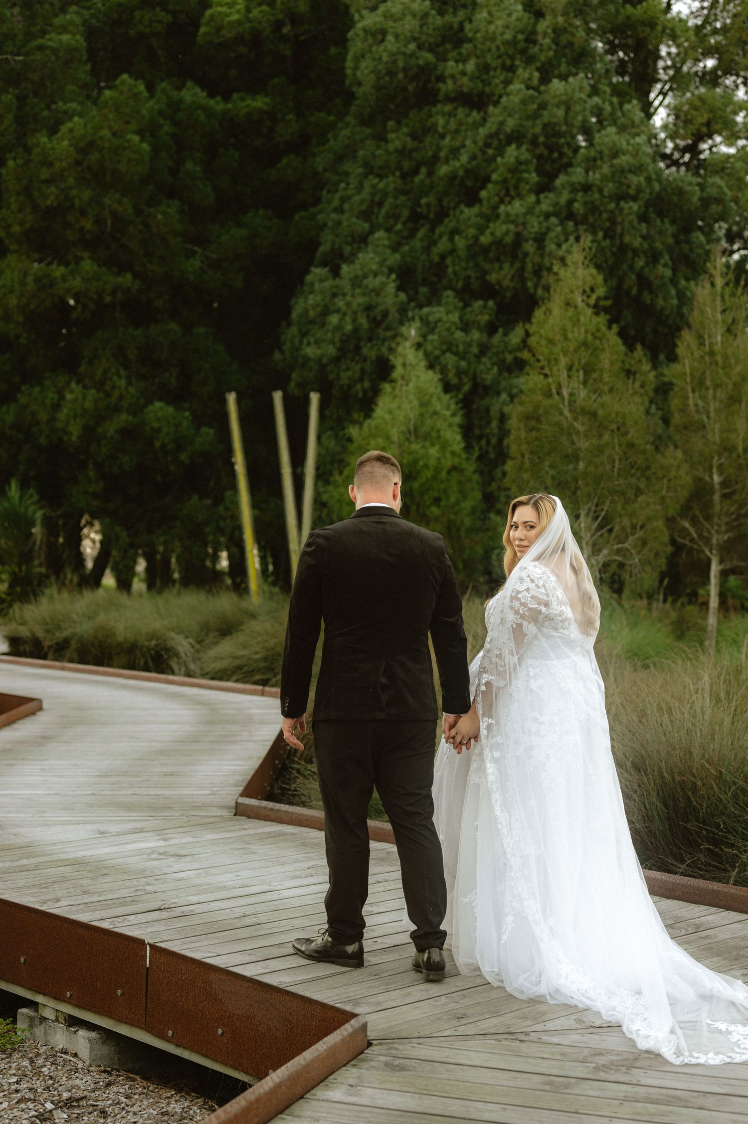 Bride and groom holding hands walking through a bridge in the forest.