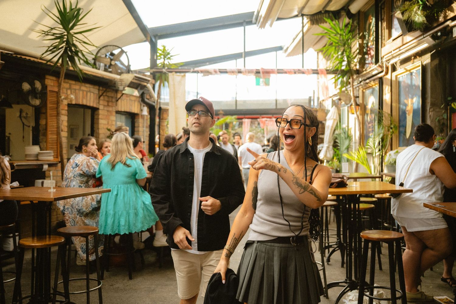 People enjoying drinks and conversation at a rustic indoor-outdoor bar with exposed brick walls and wooden furnishings.