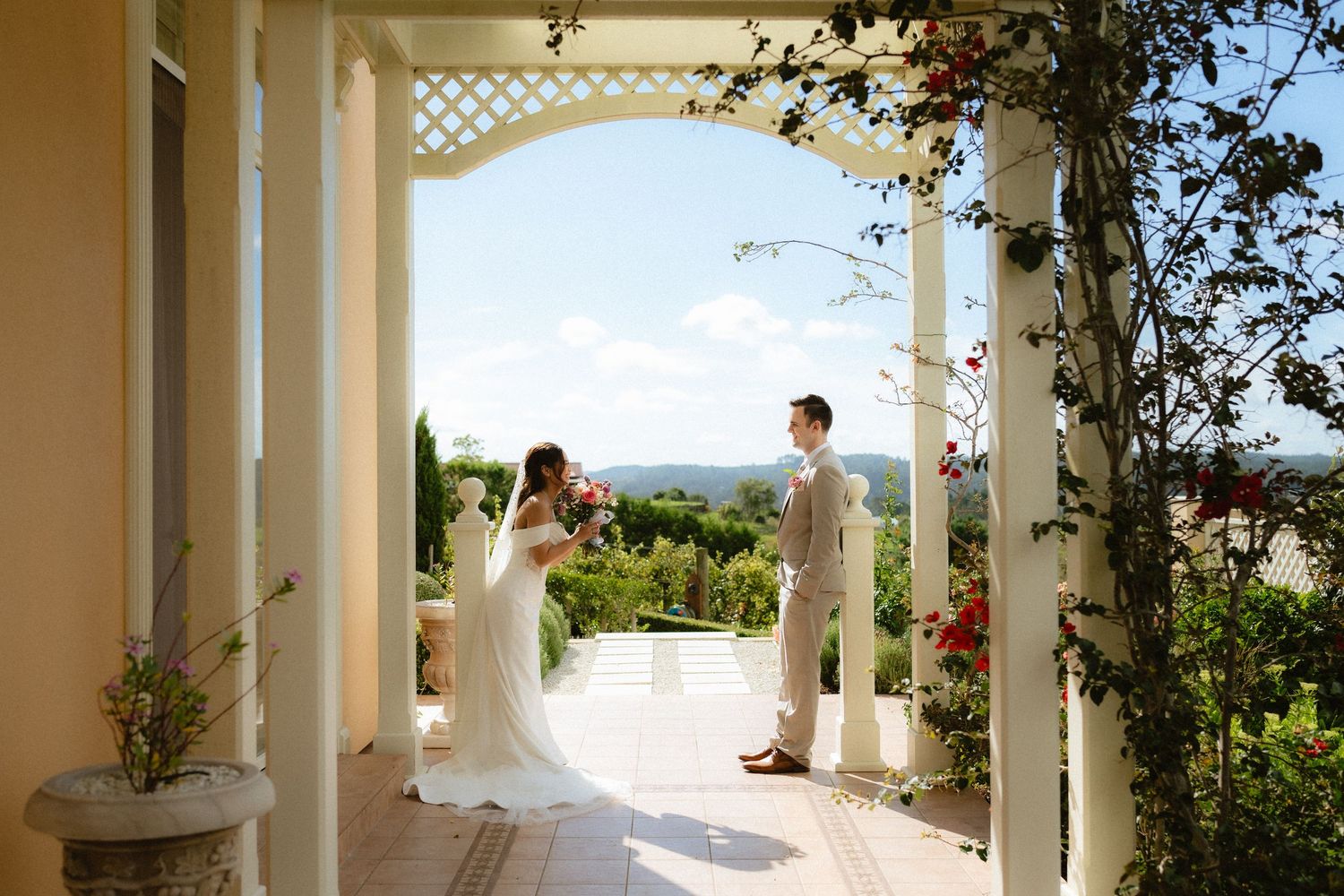 Bride and groom share a romantic first look on an elegant villa porch surrounded by lush gardens and scenic views.