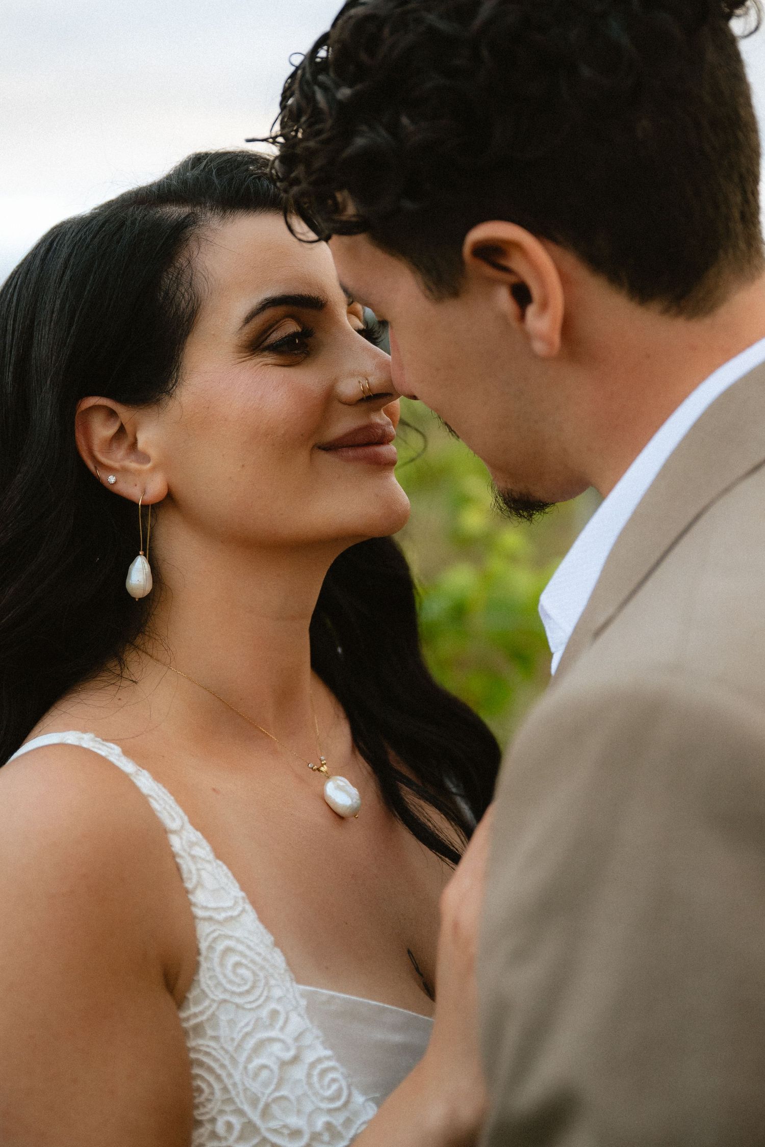 Bride and groom share a romantic moment, woman wearing pearl drop earrings and necklace in white lace wedding dress.