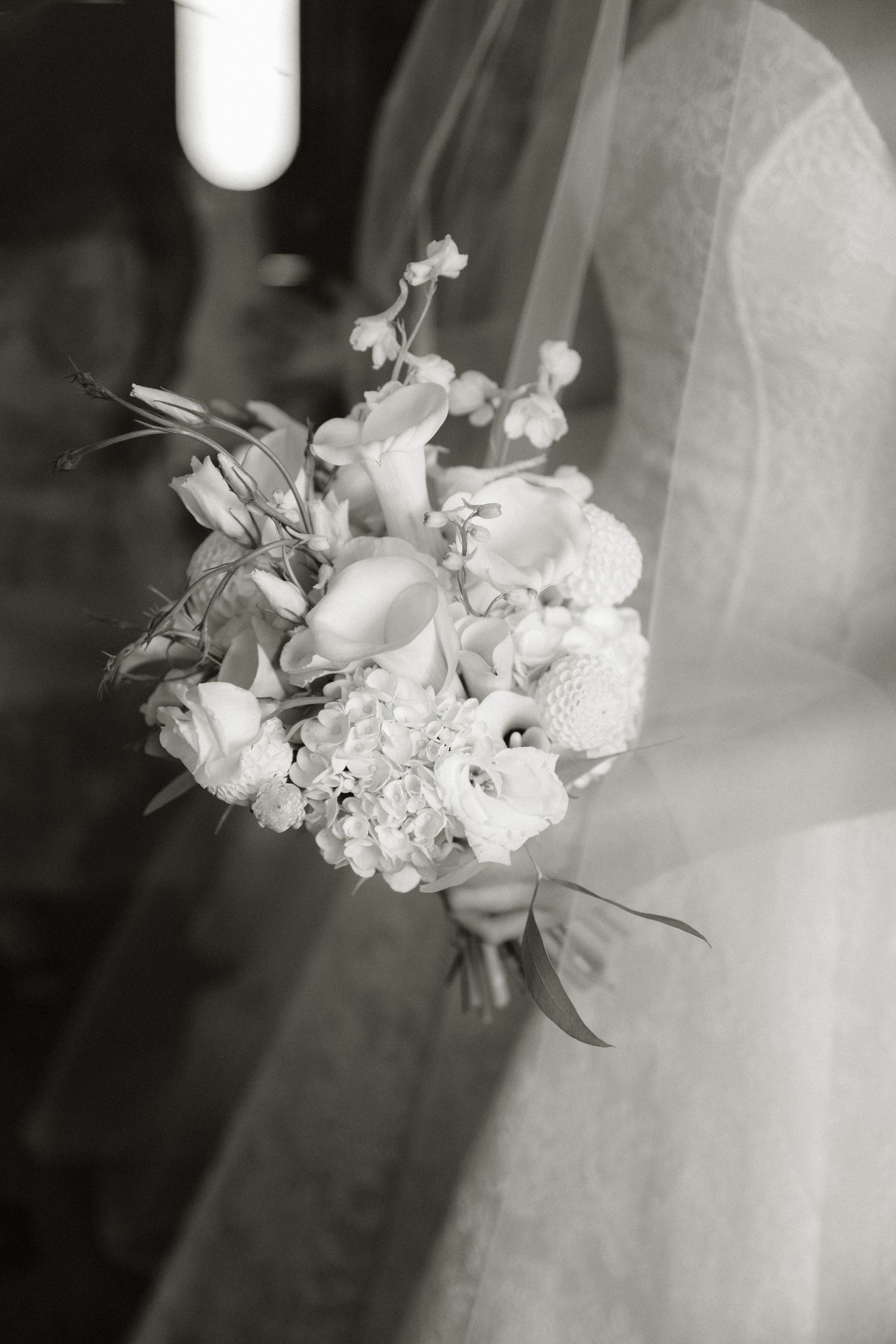 Black and white photo of a bride holding an elegant wedding bouquet with roses, calla lilies, and hydrangeas.