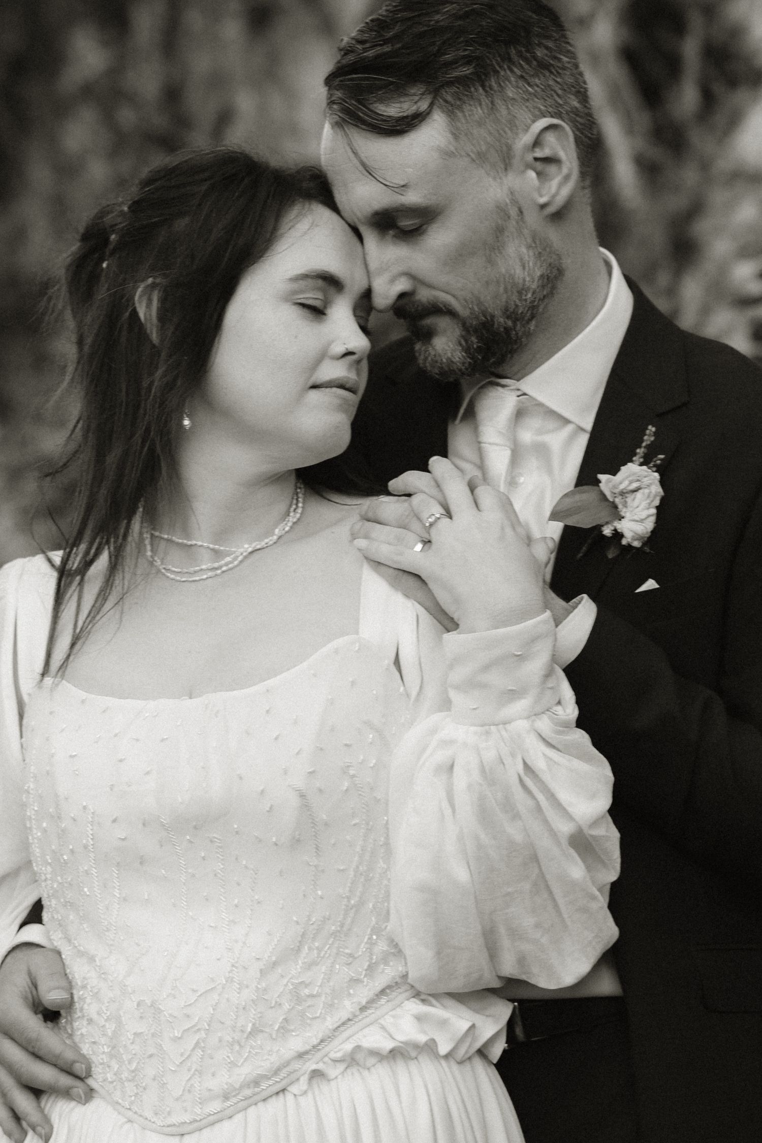 Black and white wedding portrait of bride and groom sharing an intimate moment, bride in lace dress with pearl necklace.
