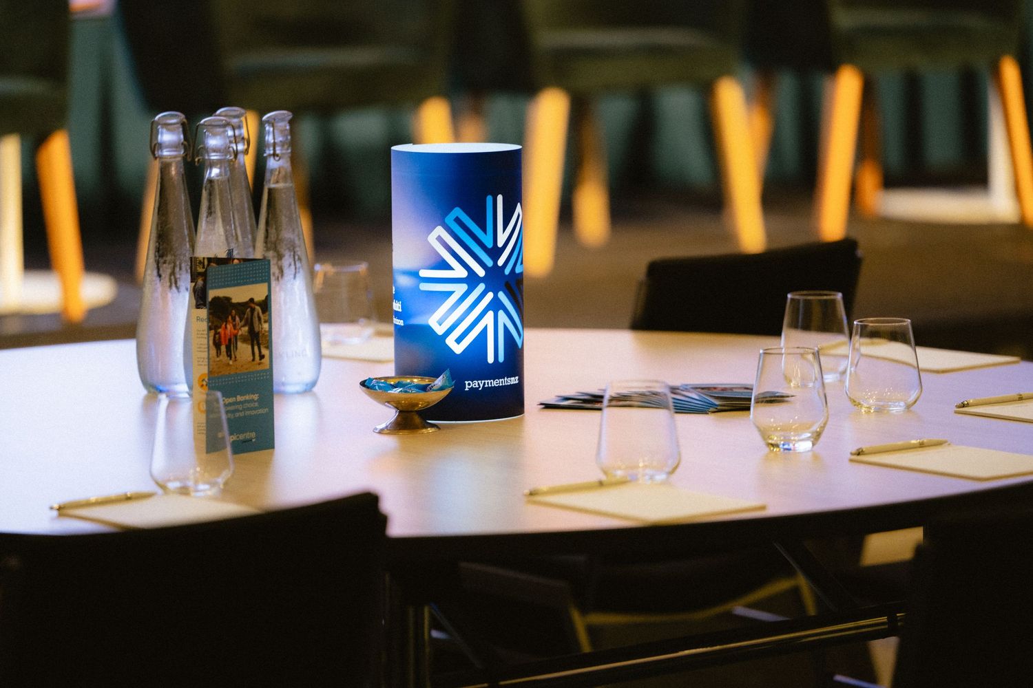 Elegant conference table setup with water bottles, branded cylinder centerpiece, and glassware in a modern venue.