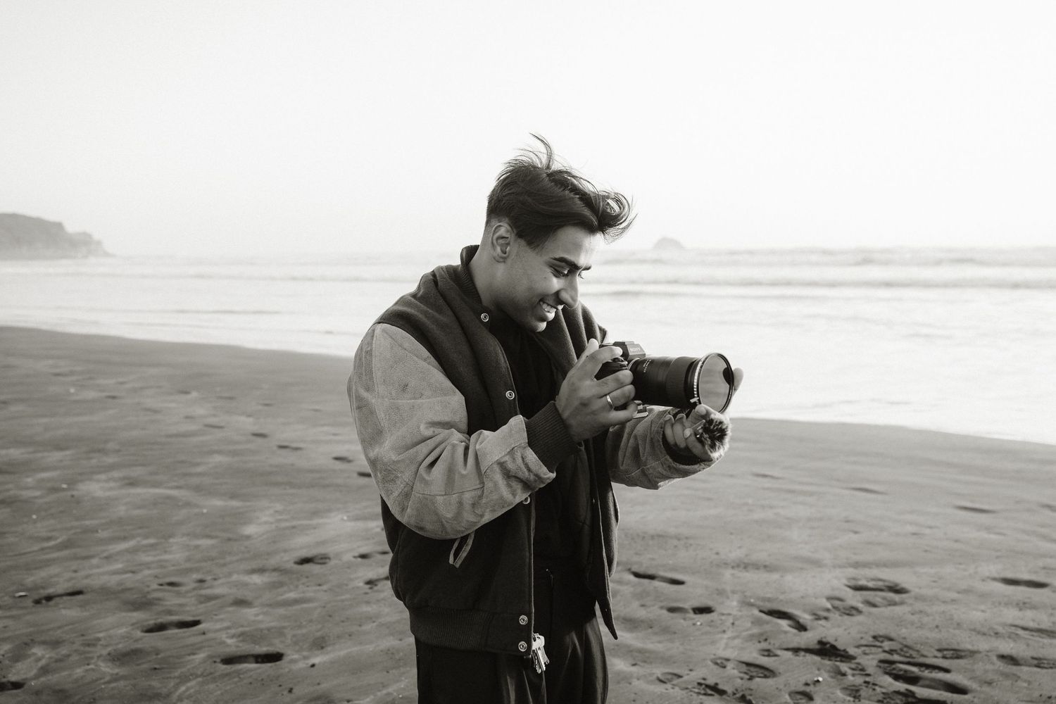 Young man reviewing photos on camera while standing on a misty beach, black and white photography.