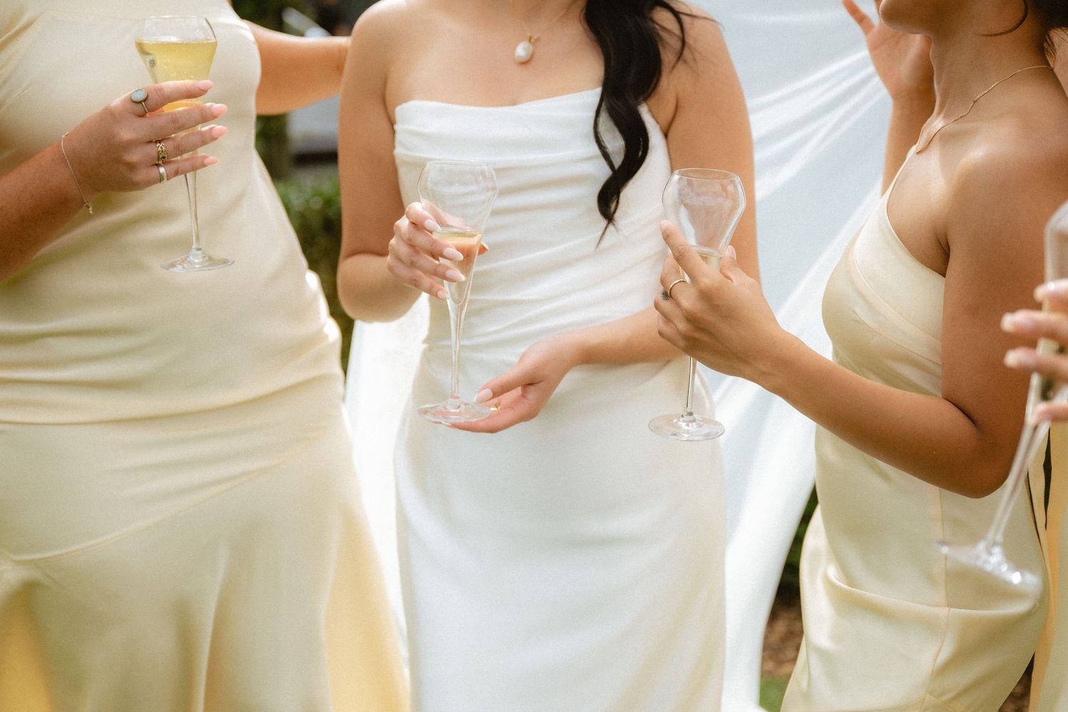 Bride in white strapless gown with bridesmaids in yellow dresses toasting champagne glasses at wedding.