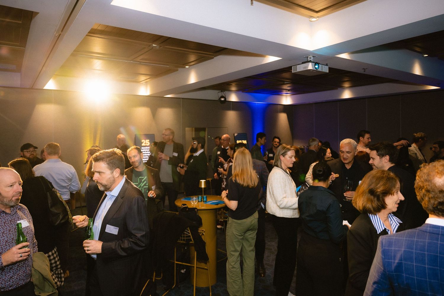 Business professionals network and socialize at a crowded indoor corporate event with ambient lighting.