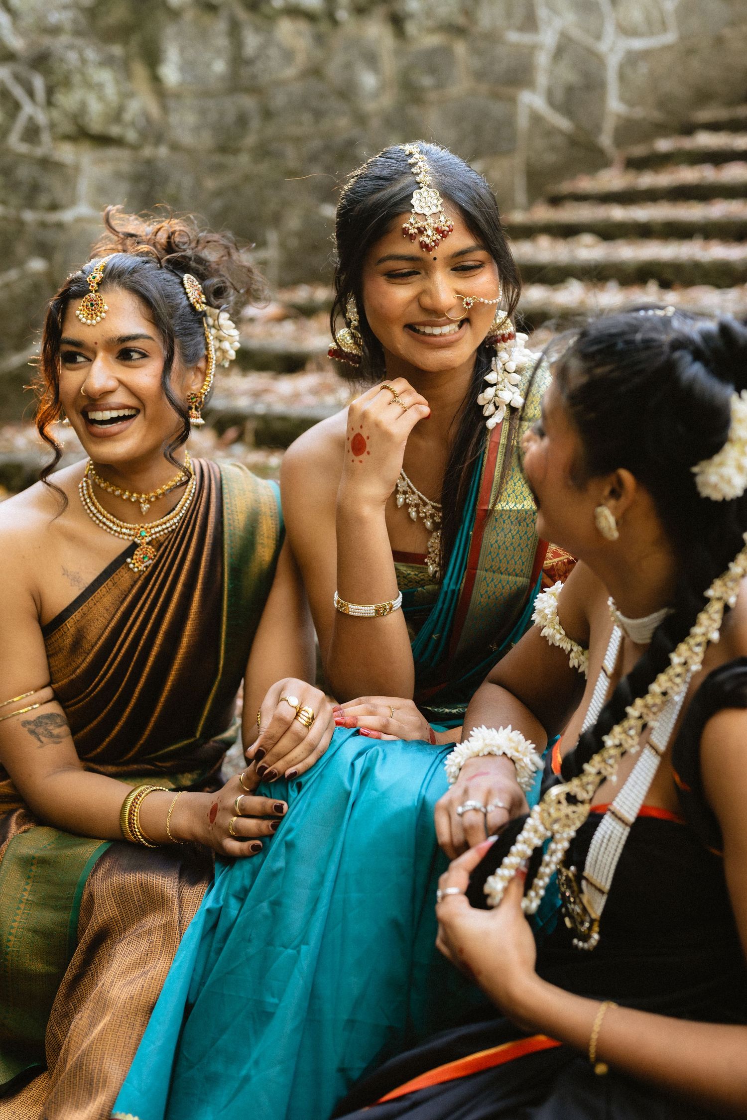 Wedding party in traditional South Asian attire poses against stone wall backdrop.