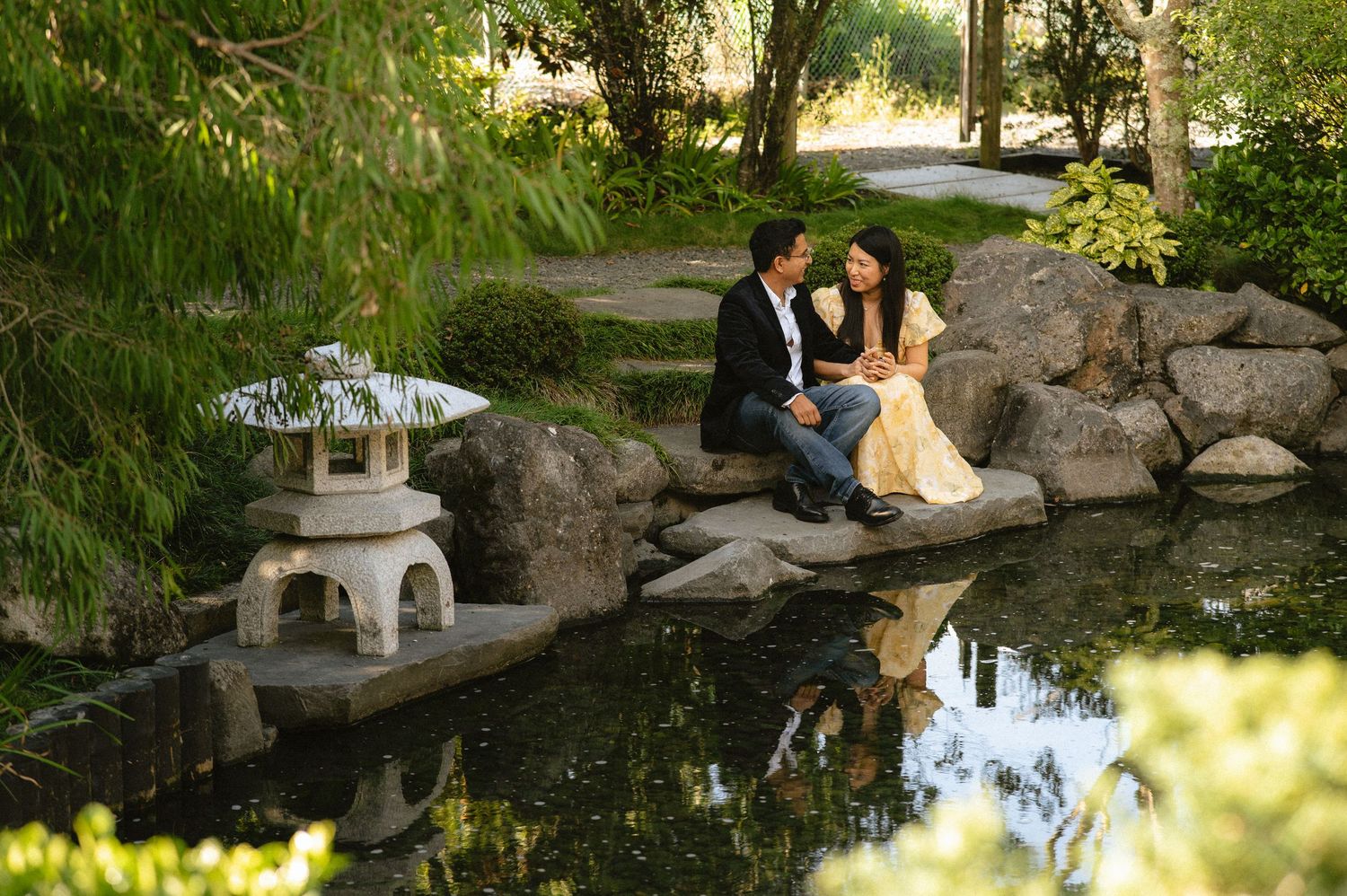 Romantic garden path with stone features and reflective pond surrounded by natural landscaping.