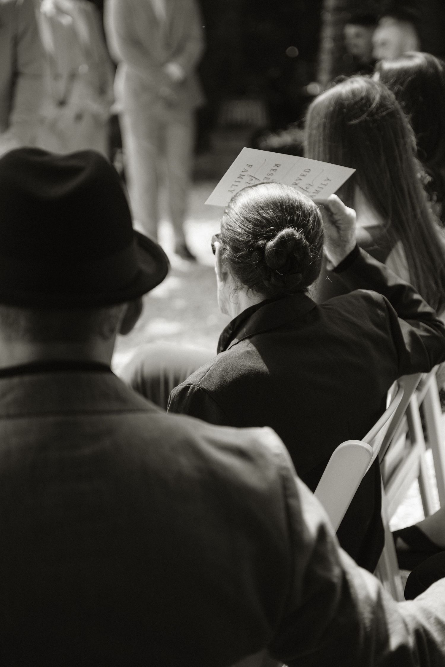 Black and white photo of seated audience members at a formal event, woman with bun holding program.