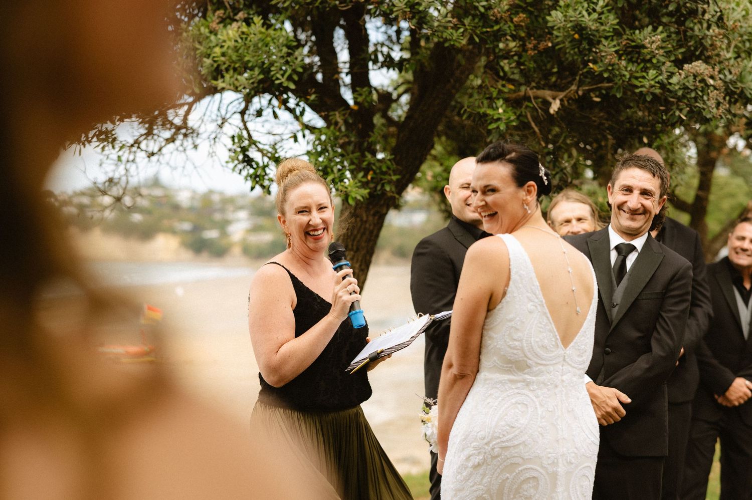 Wedding party members sharing joyful moments outdoors under trees.
