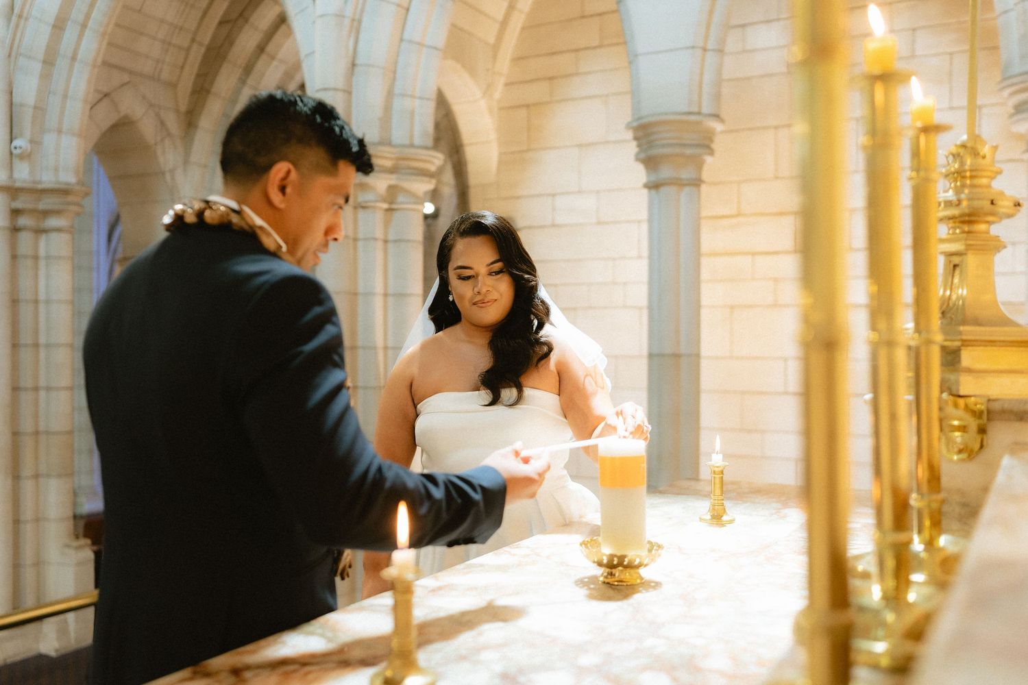 Bride and groom lighting unity candles during a wedding ceremony in an elegant church with golden accents.
