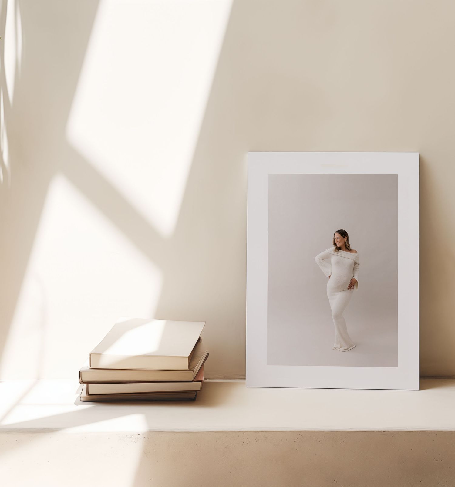 A minimalist composition of white art frames and books arranged against a beige wall with dramatic natural lighting.