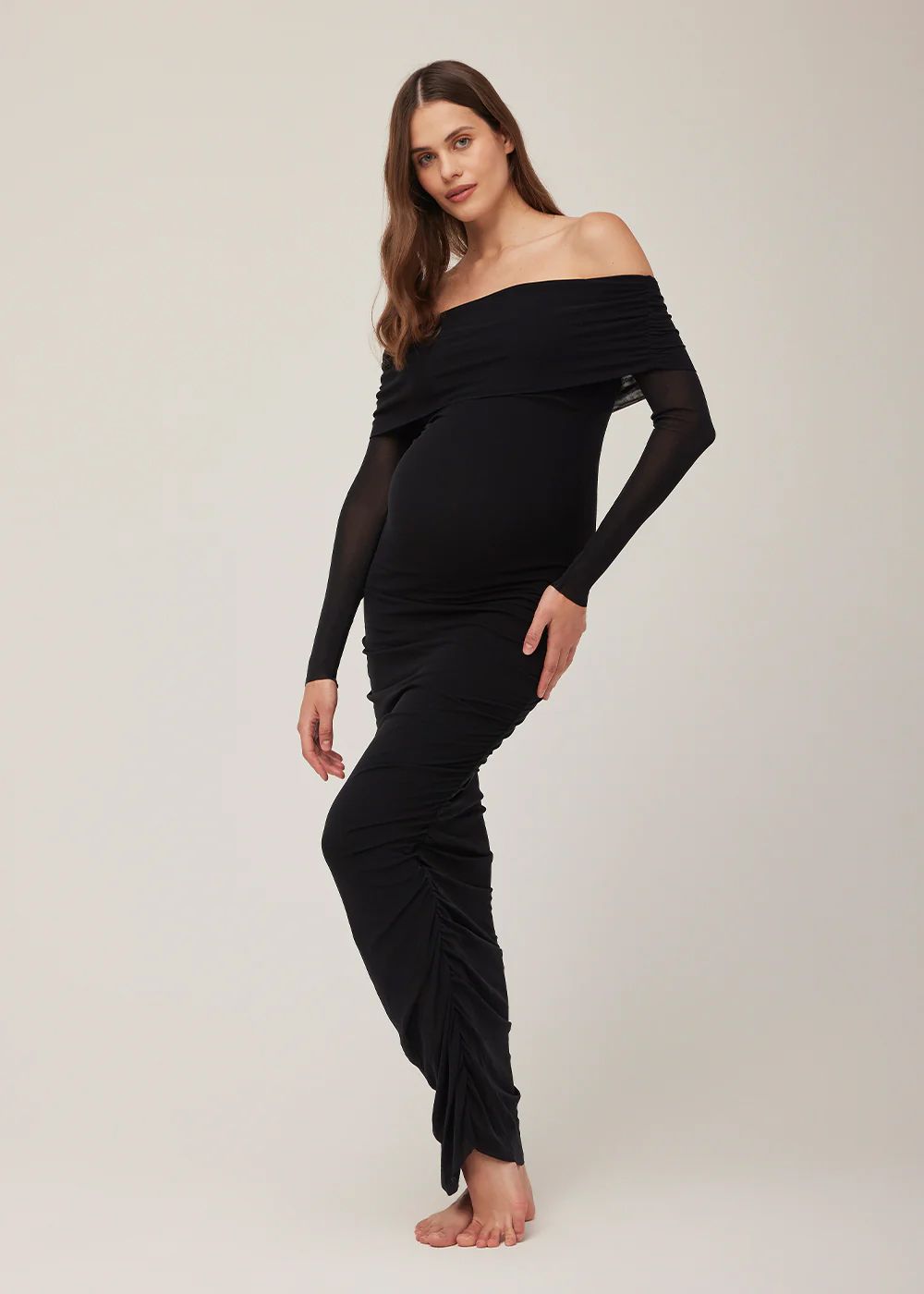 Black off-shoulder maternity maxi dress with ruched sides and sheer long sleeves, worn by a model.