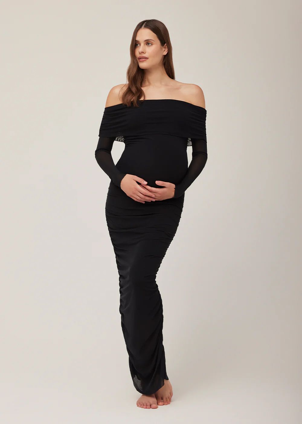 Pregnant woman wearing a black off-shoulder long sleeve maxi dress, showcasing a form-fitting maternity style.