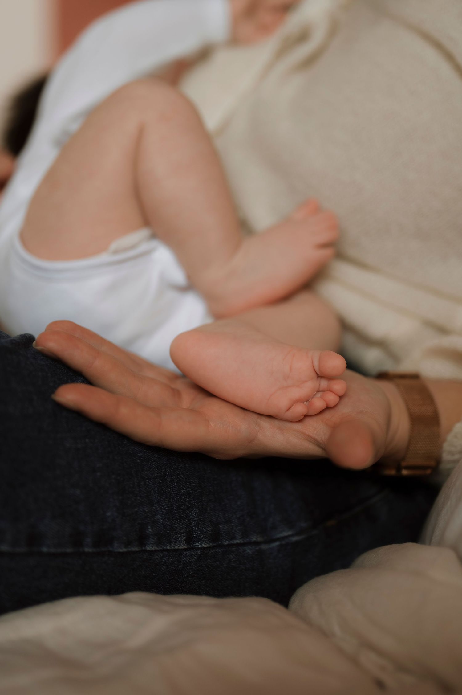 A tiny baby's foot rests gently in an adult's palm while sitting on dark denim jeans.
