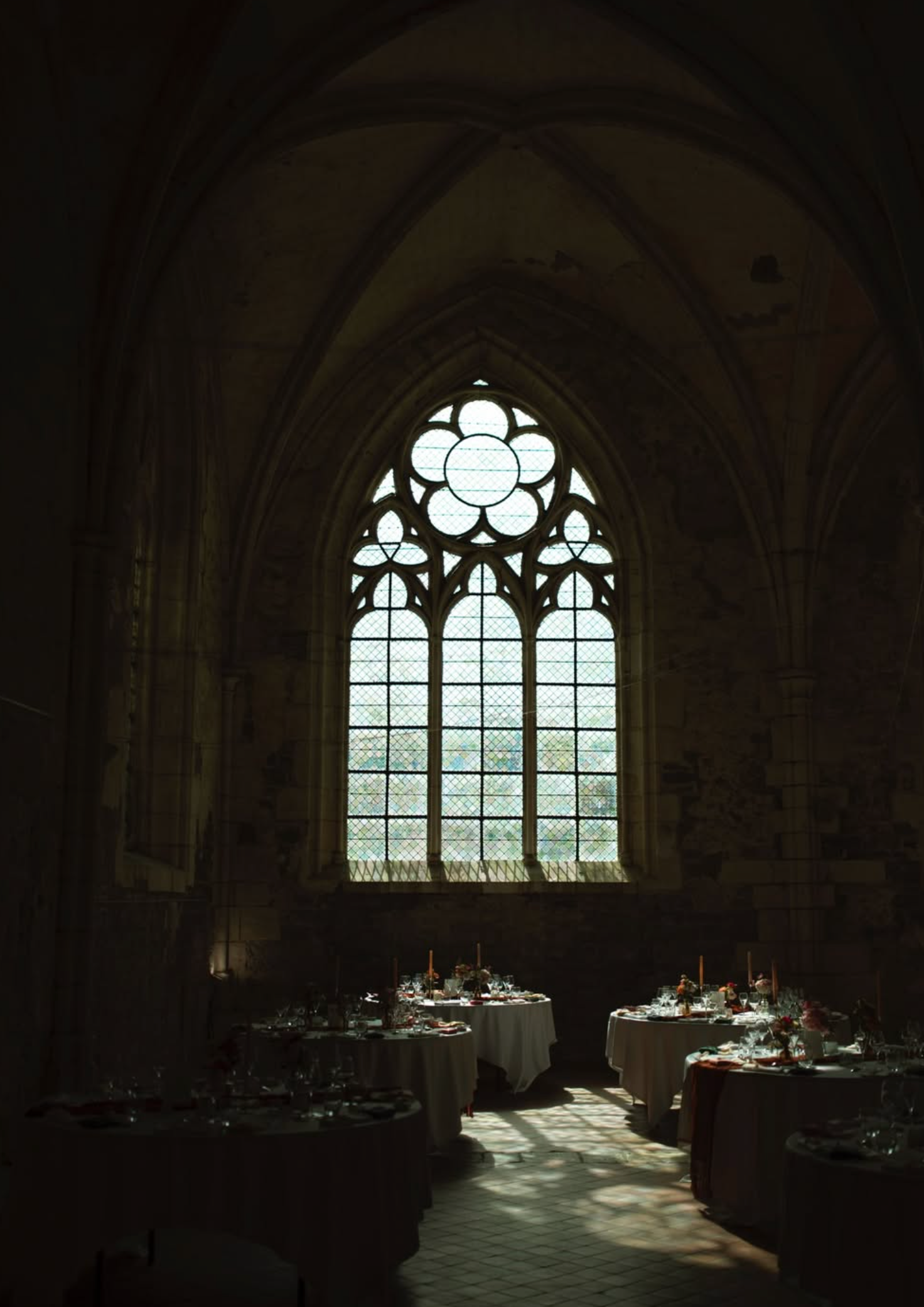 Gothic cathedral interior with arched stained glass window illuminating elegant dining tables set for a formal event.