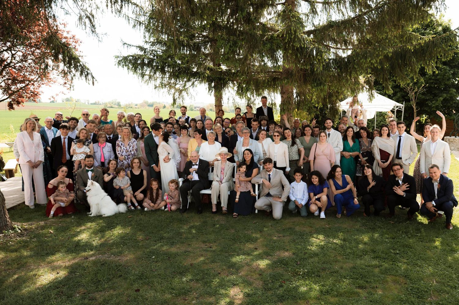Large group gathered outdoors for a special event photo under trees on a sunny day.