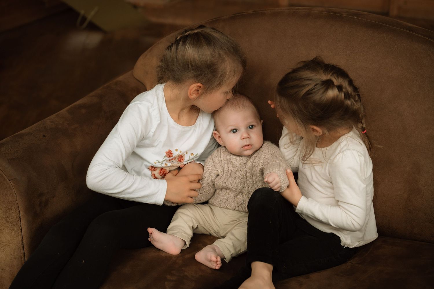 A series of connected sepia-toned photographs showing tender moments between a baby and caregiver on a couch.