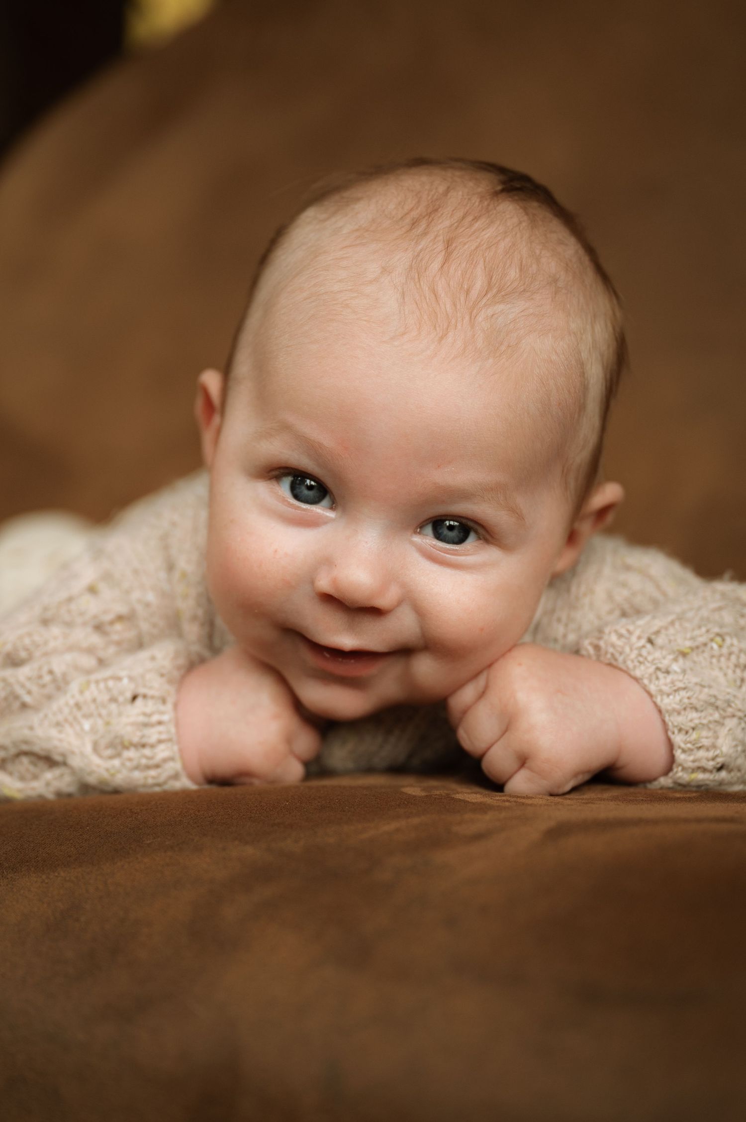 A sequence of photos showing a baby peeking and smiling from under a cream-colored blanket in warm lighting.