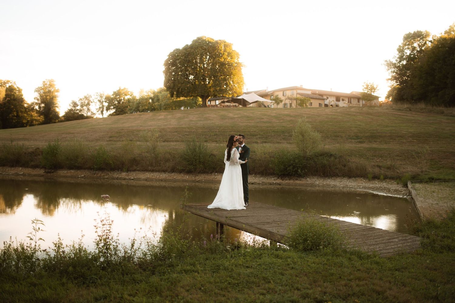 A romantic sunset wedding photoshoot in a golden field with a pond reflecting the warm evening light.