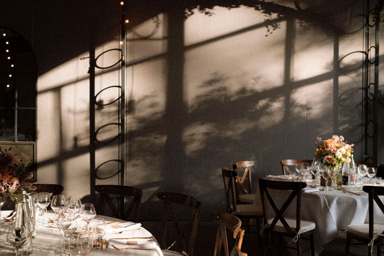 Elegant wedding reception venue with dramatic shadow patterns on walls, white tablecloths, and floral centerpieces.