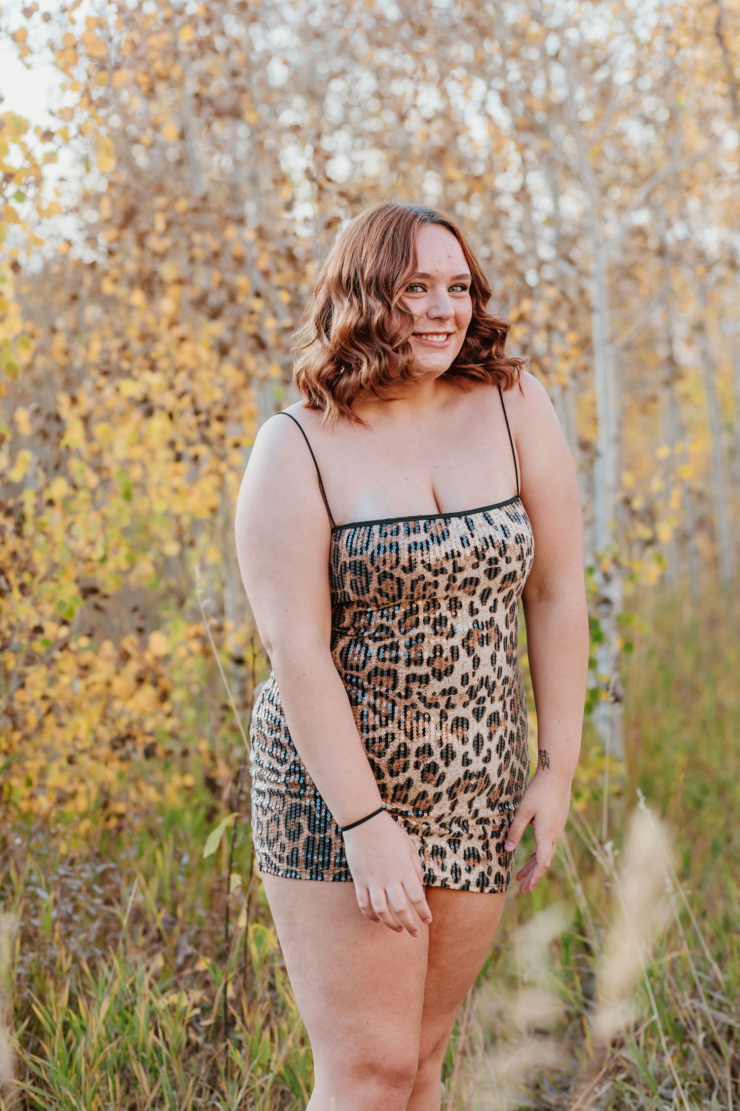 A person in a leopard print romper poses outdoors against golden autumn foliage.