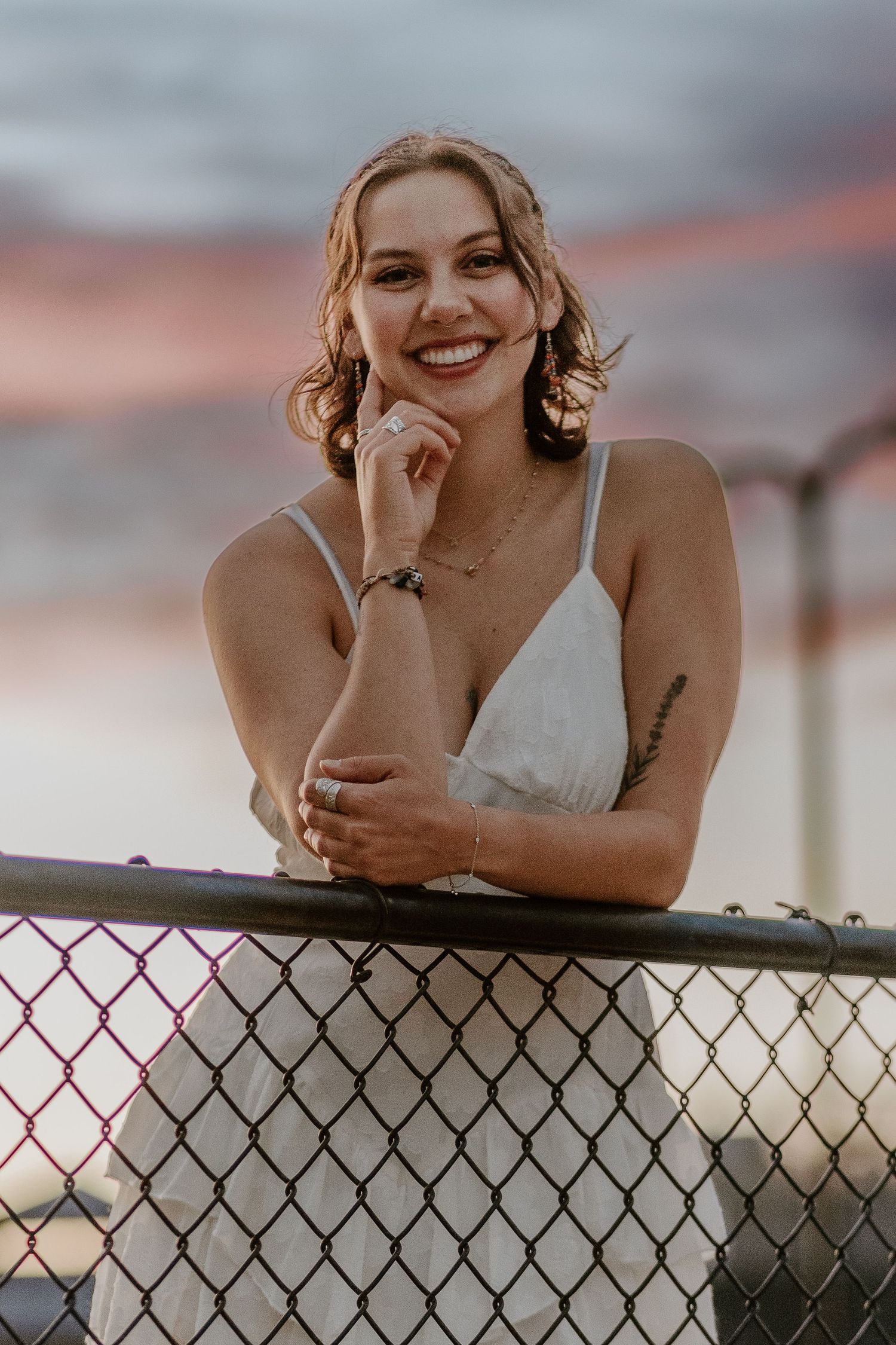 A portrait against a sunset sky with chain link fence in the foreground.