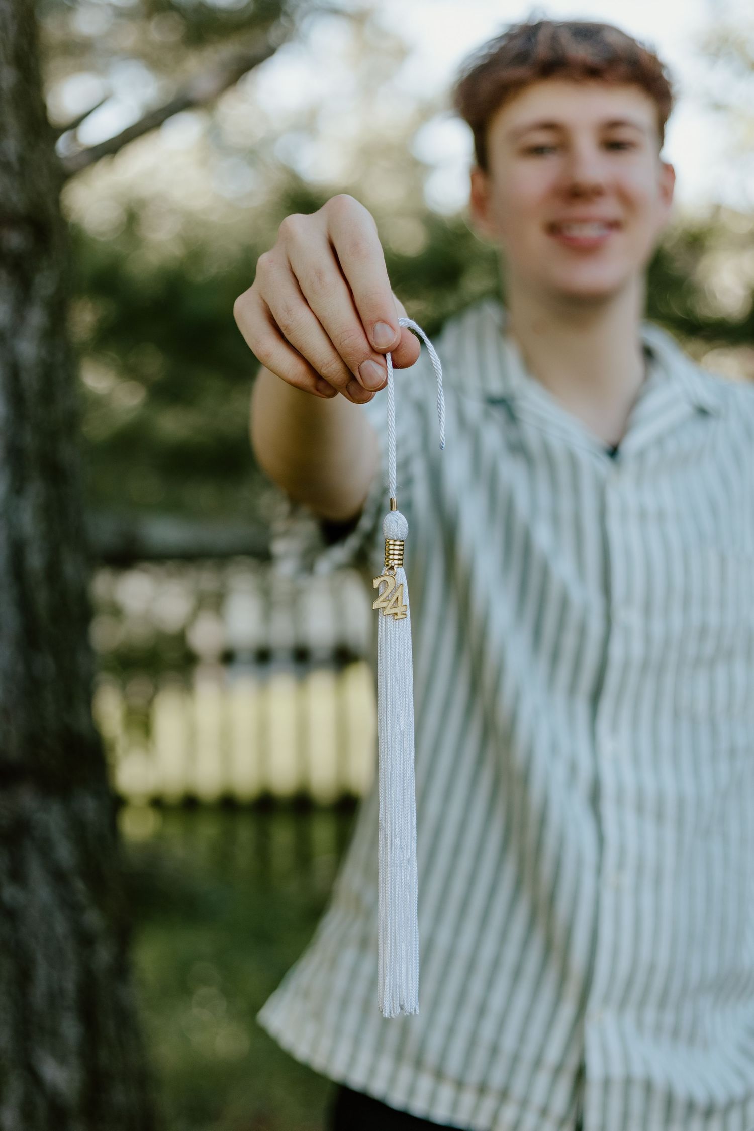 A hand holds up a white graduation tassel against a blurred outdoor background.
