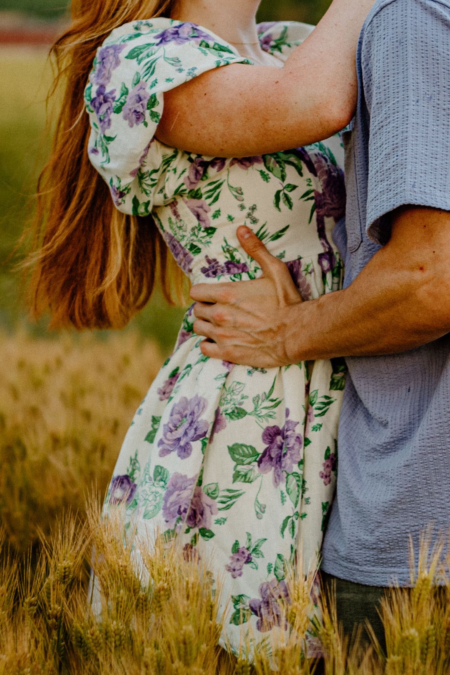 A romantic embrace captured in a field with the woman wearing a floral dress and man in grey.