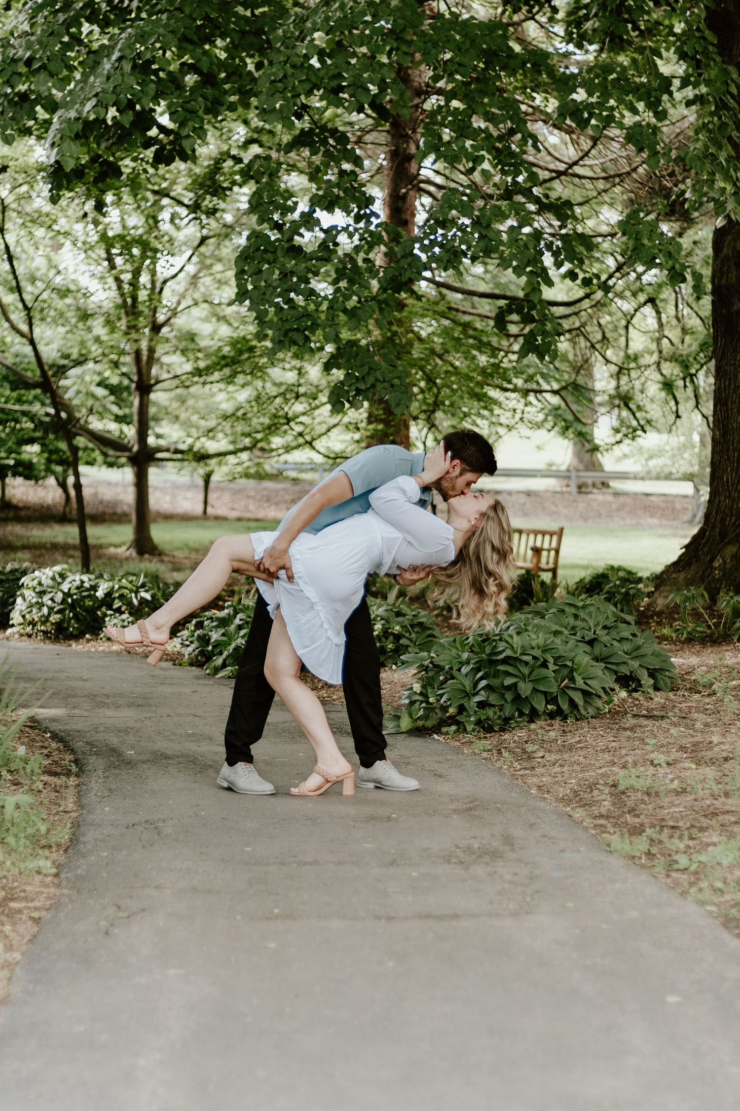 A romantic dip pose on a garden path surrounded by lush green trees.