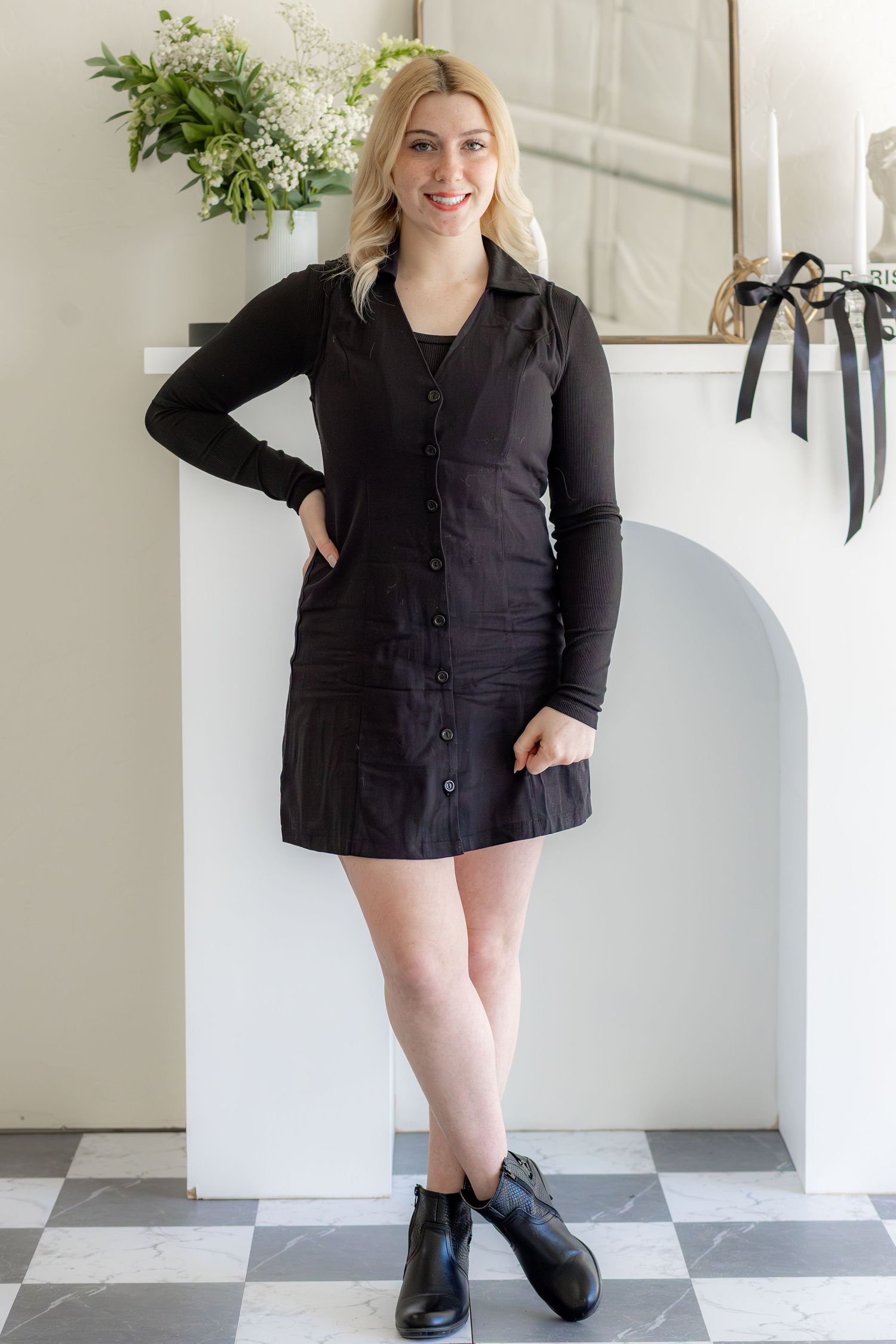 Professional headshot in modern studio with black button-down dress and boots.