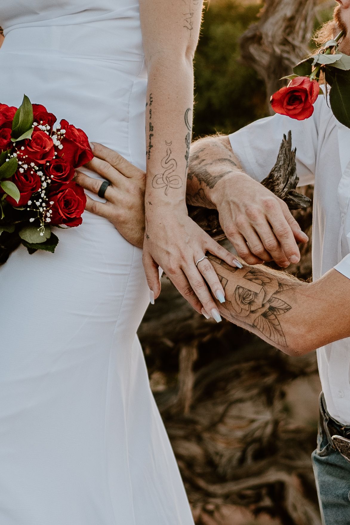 A close-up of hands holding red roses with matching tattoos visible on both arms.