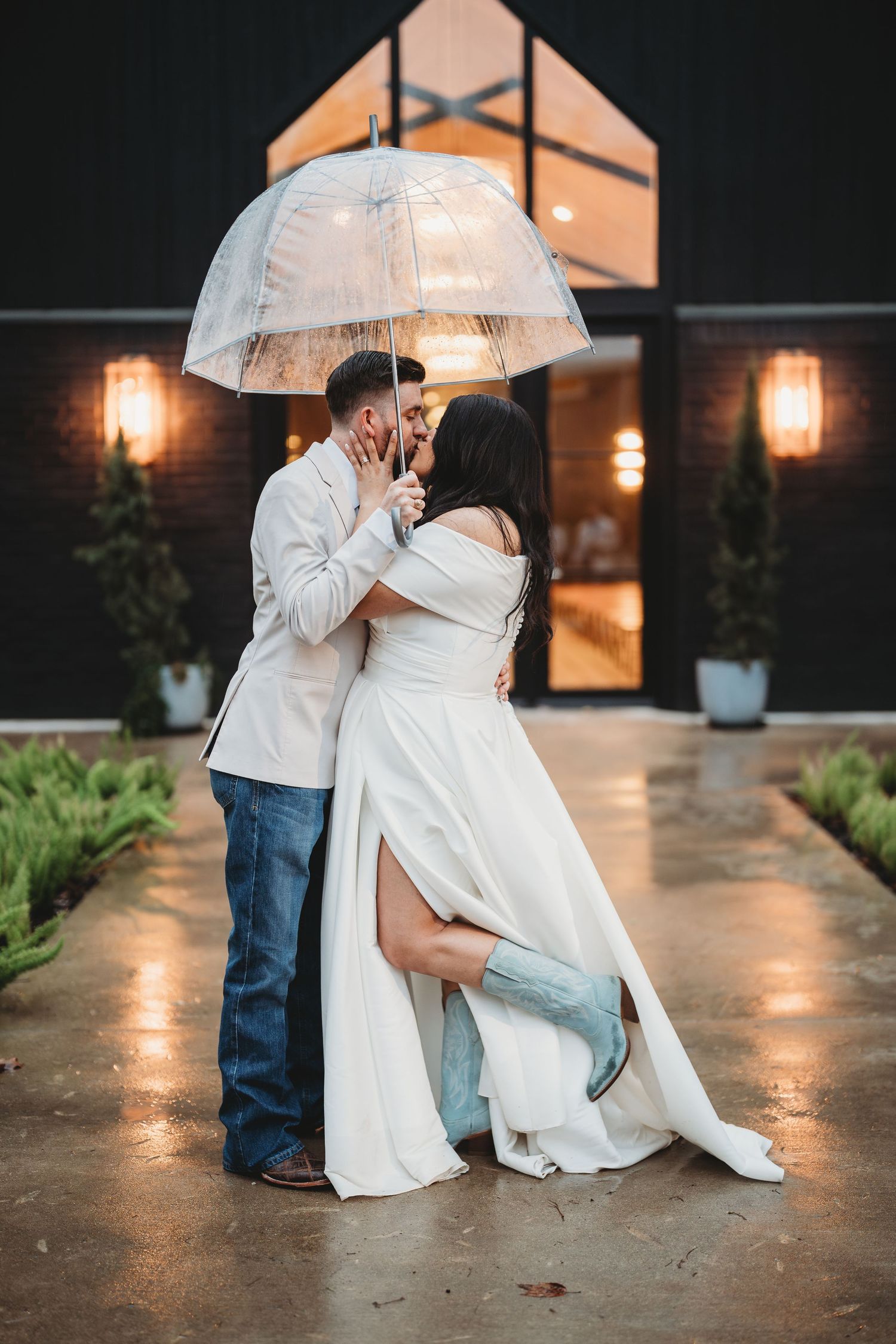 Bride and groom sharing a kiss under a clear umbrella in the rain on their wedding day | East Texas wedding photographer