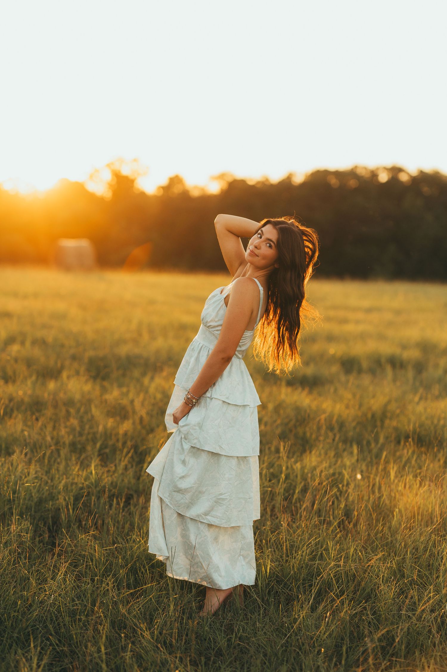 East Texas senior girl in a white dress posing in a golden field at sunset