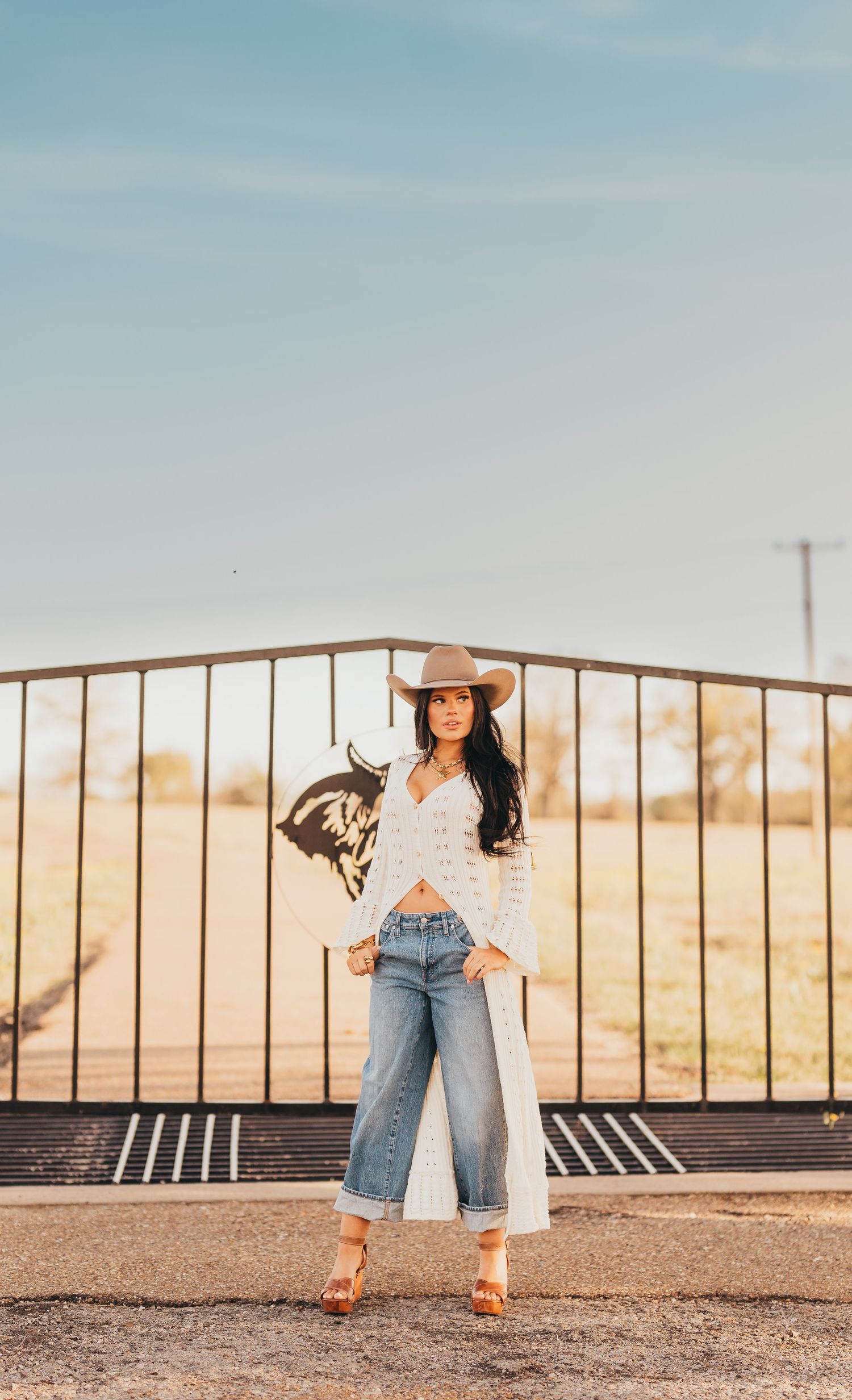 East Texas senior girl in jeans and a white top posing by a metal railing at golden hour