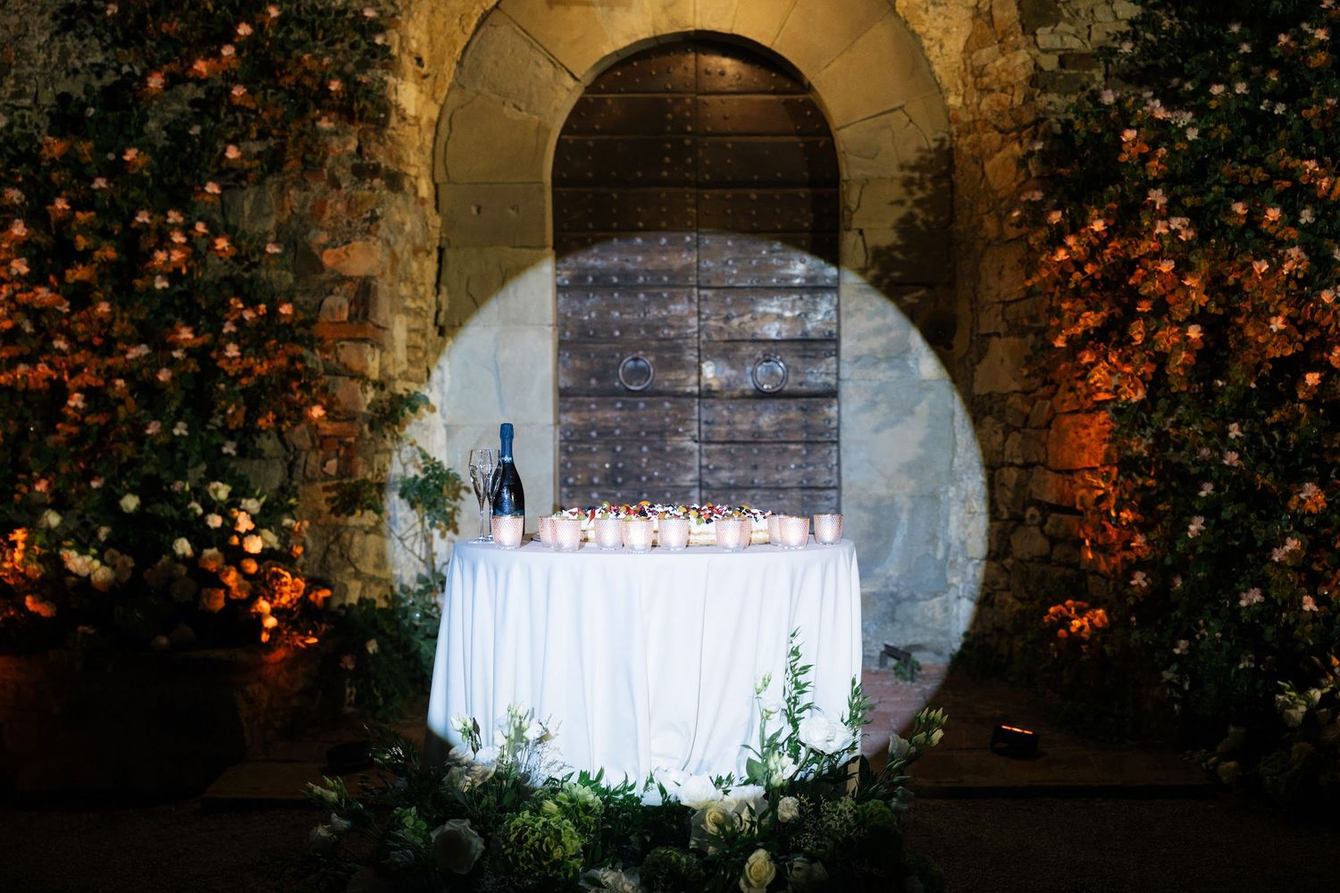 Champagne tower on draped table framed by floral arrangements at Italian castle wedding.