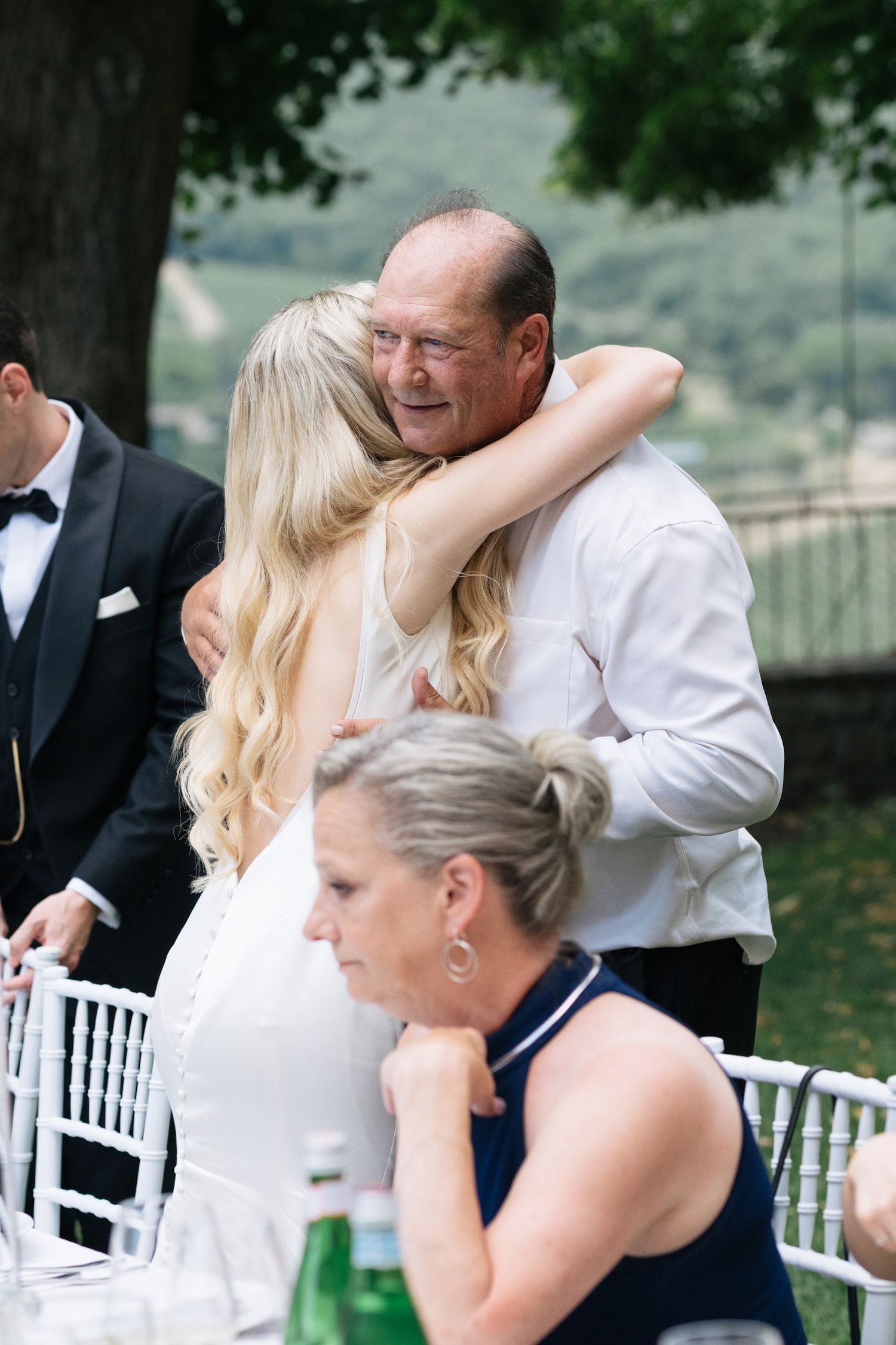Bride shares an emotional hug with a family member during an outdoor Tuscan wedding reception.