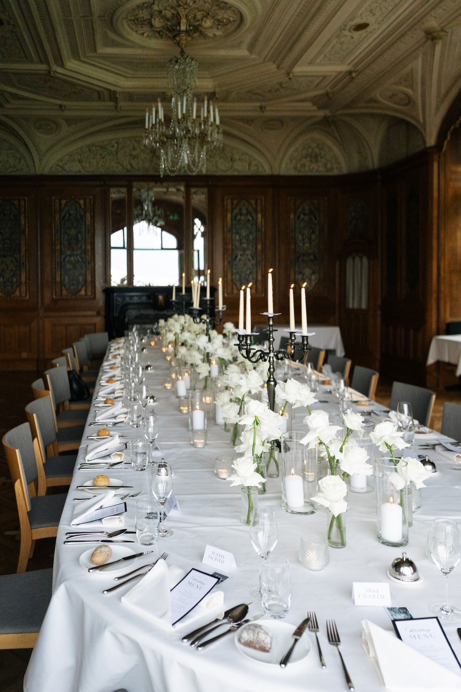 Elegant long wedding reception table with white floral centerpieces, candelabras, and crystal chandelier.