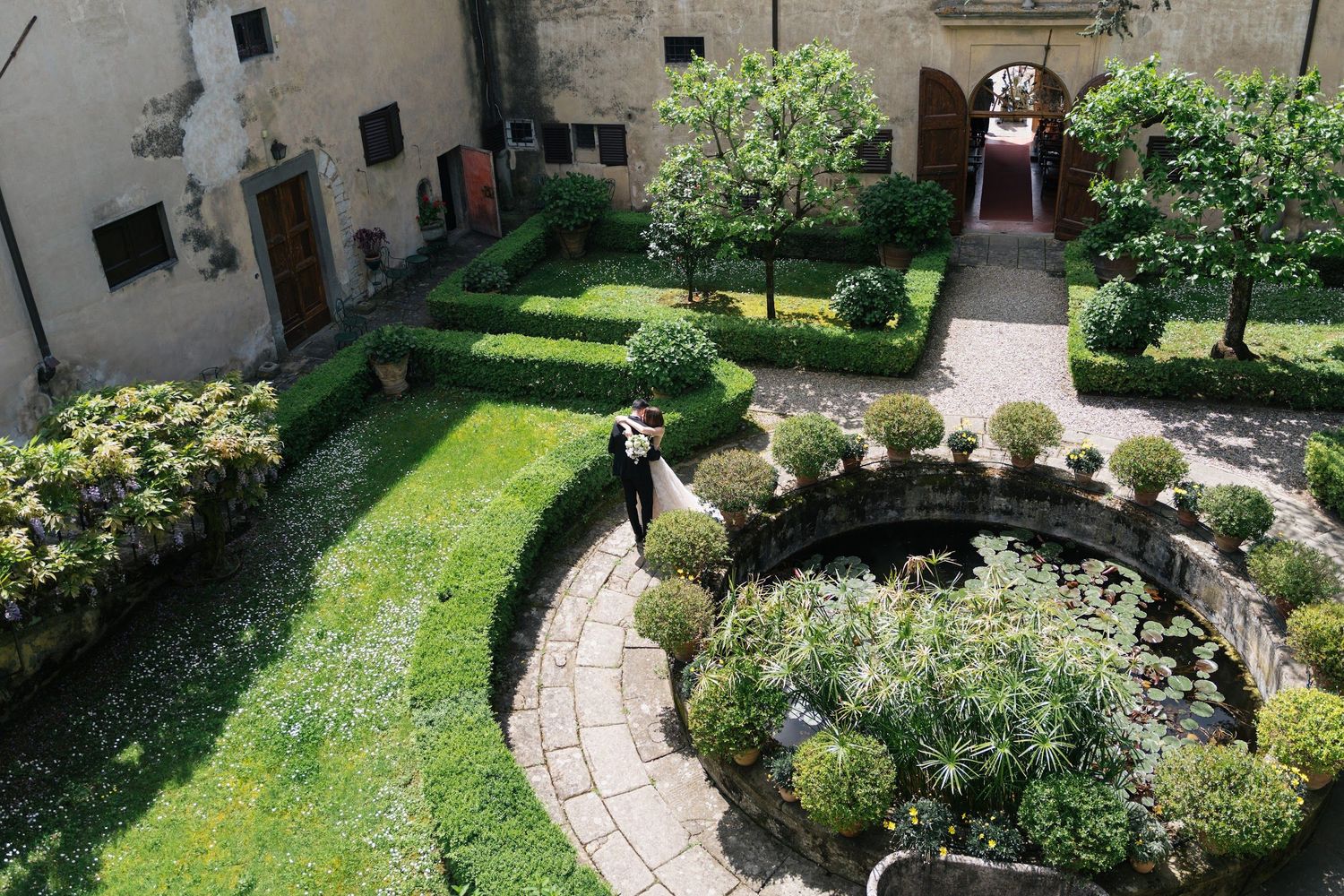 Aerial view of couple walking through a lush formal garden courtyard at a wedding venue.