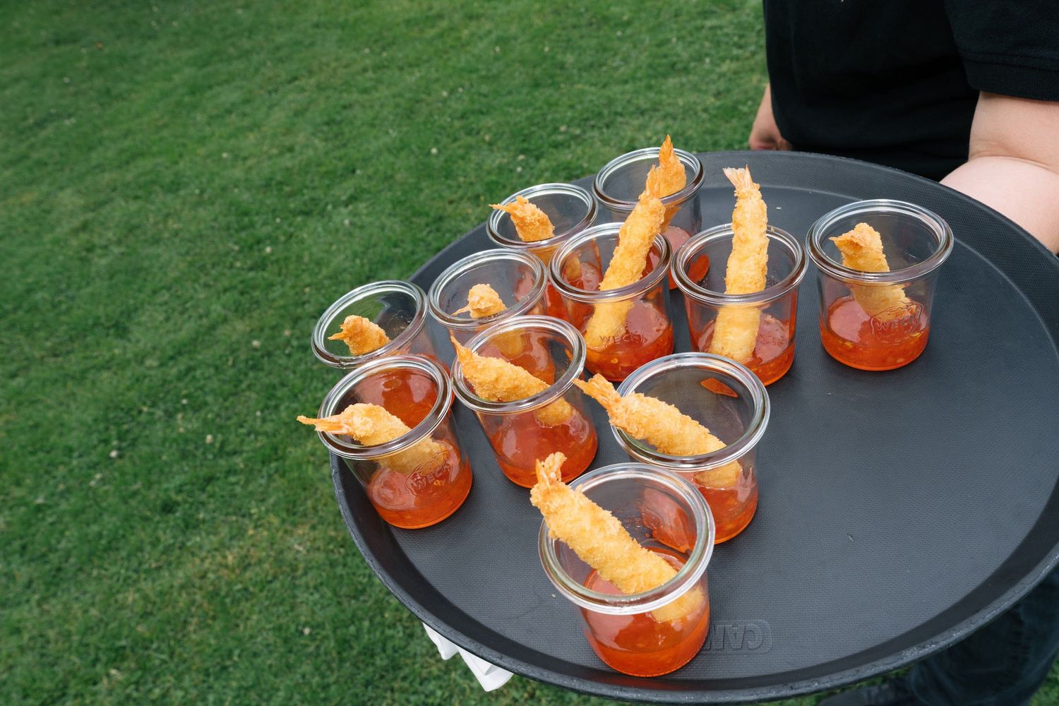 Elegant wedding appetizers of tempura shrimp cocktail shots served on a round black tray.