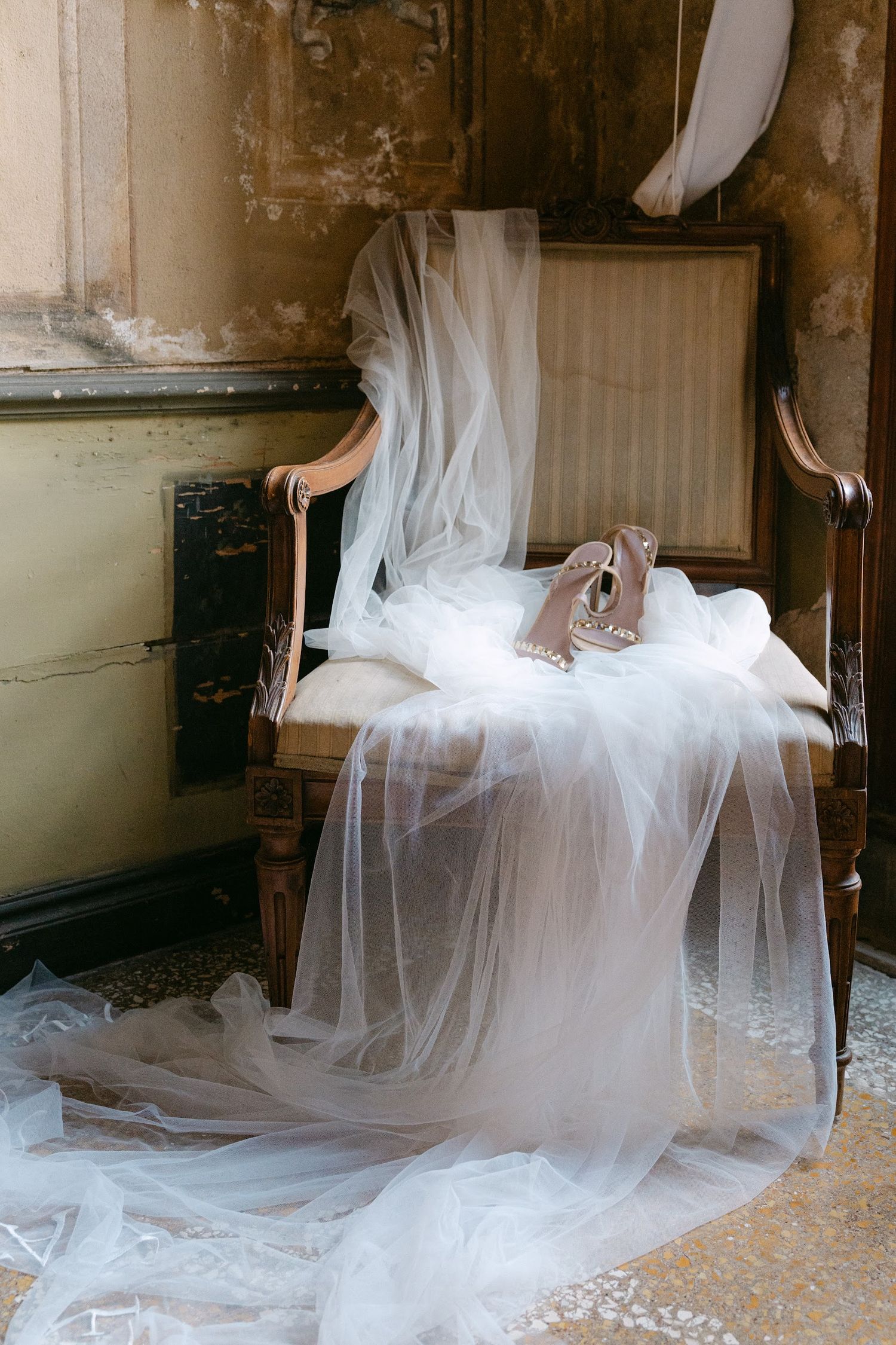 Bridal veil and heels draped over antique chair in rustic vintage interior setting.