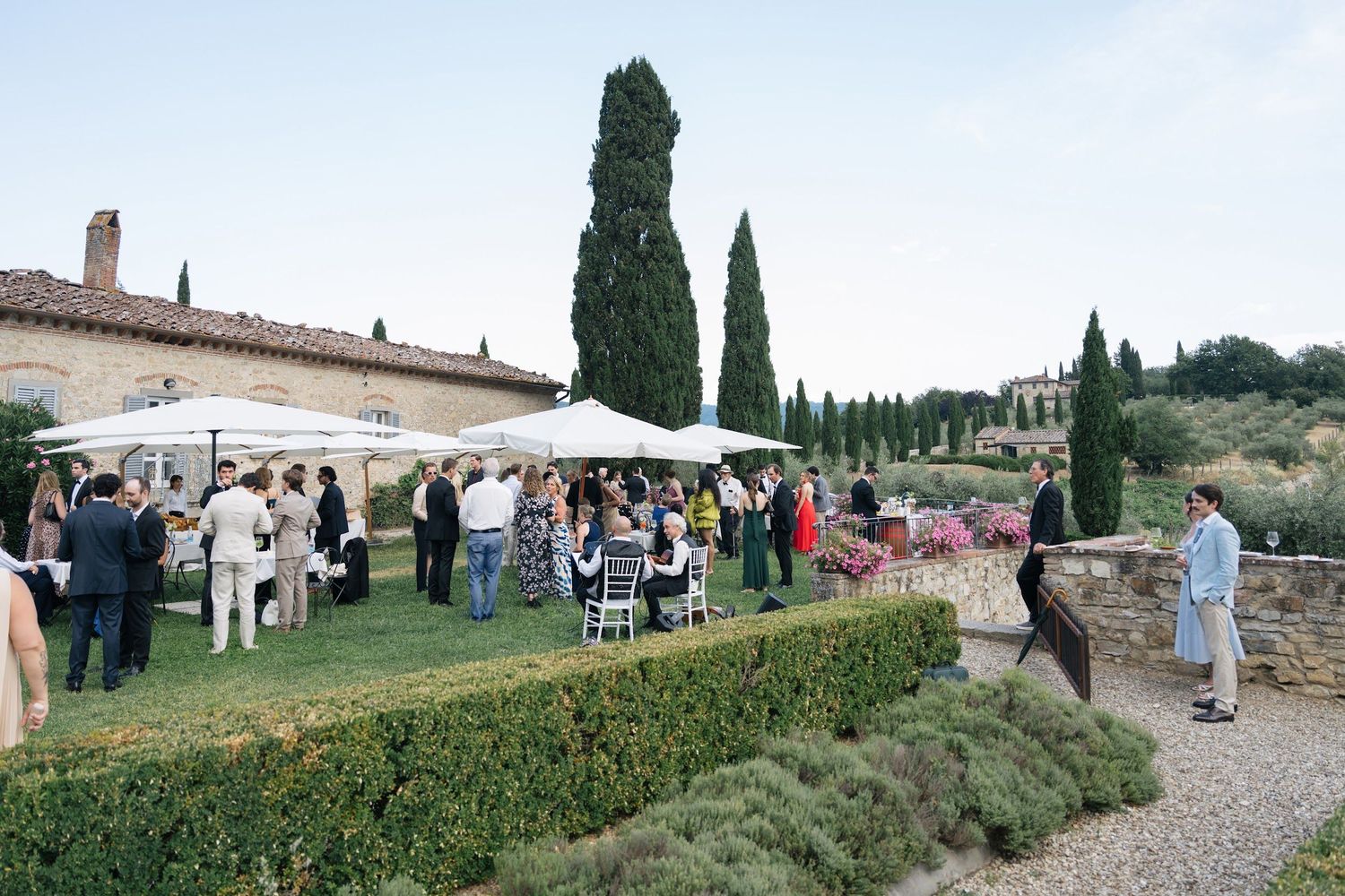 Elegant outdoor wedding cocktail hour at a Tuscan villa with guests mingling under white umbrellas.