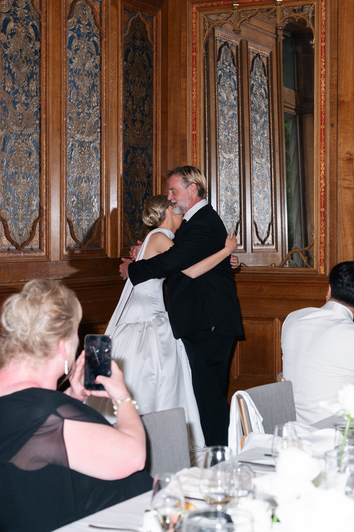 Bride in white gown shares a father-daughter dance at elegant wood-paneled wedding reception.