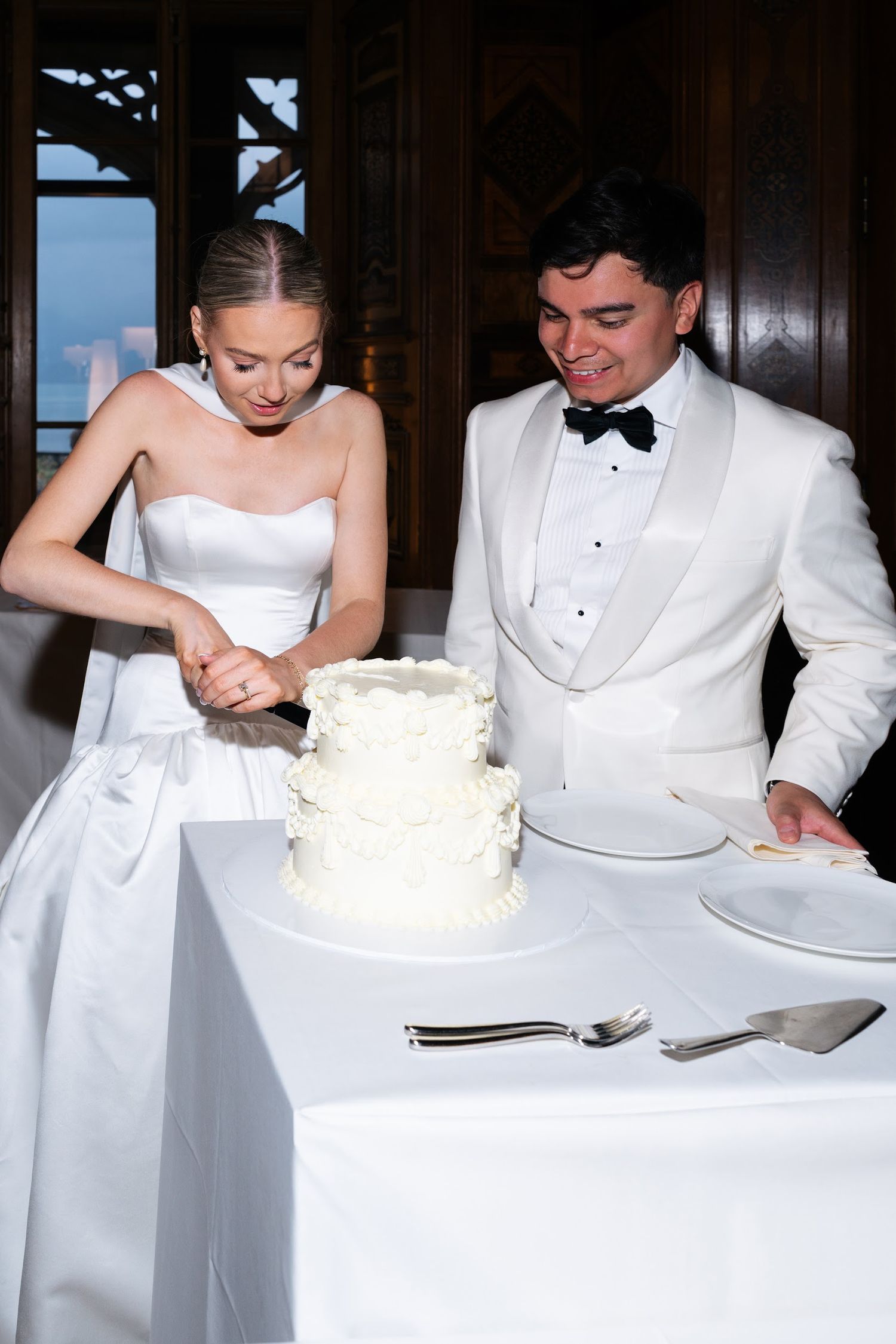 Bride and groom cutting their two-tier white wedding cake at their elegant reception.