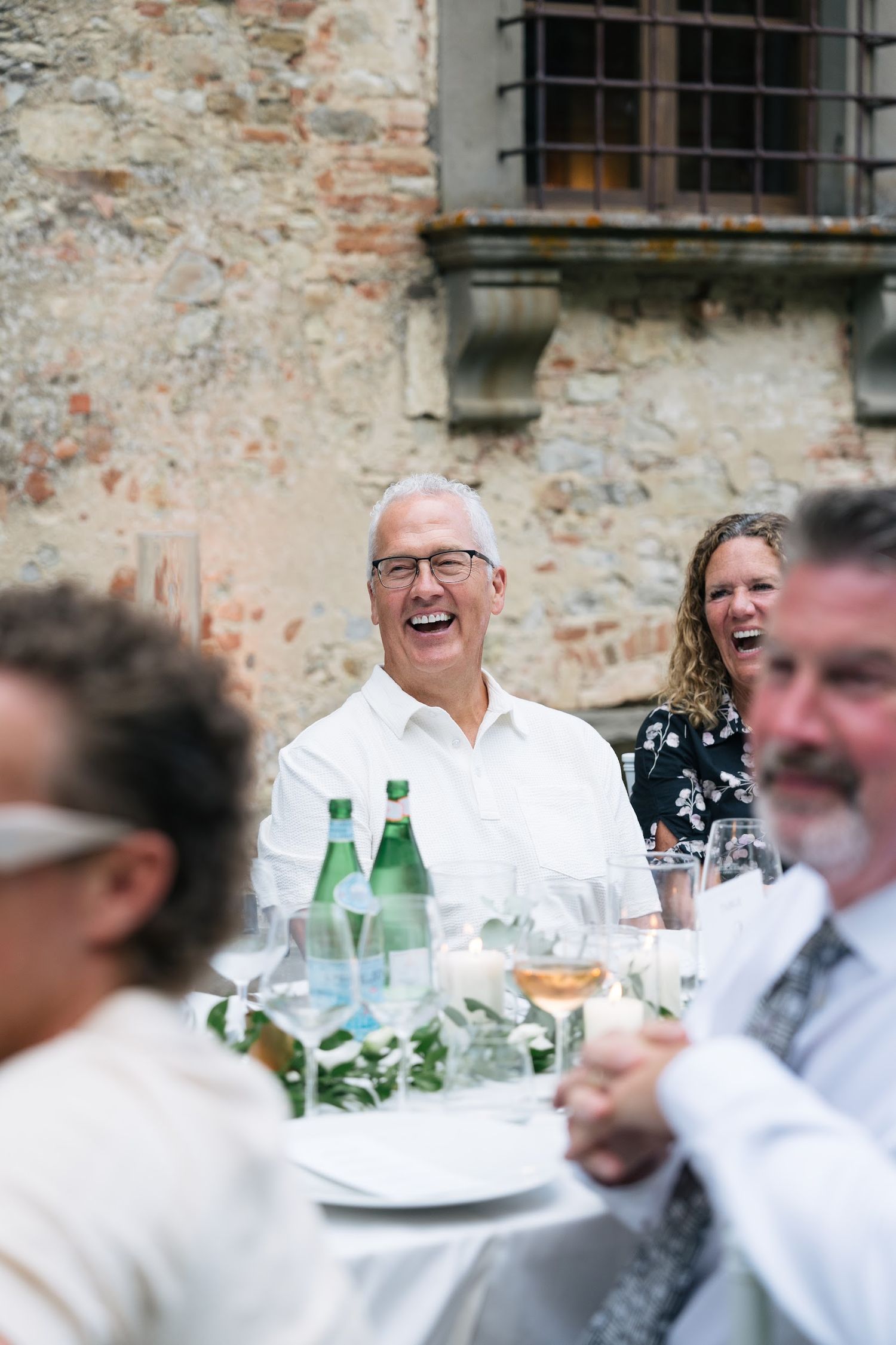 Wedding guest laughs joyfully during speeches at an outdoor Italian castle wedding reception dinner.