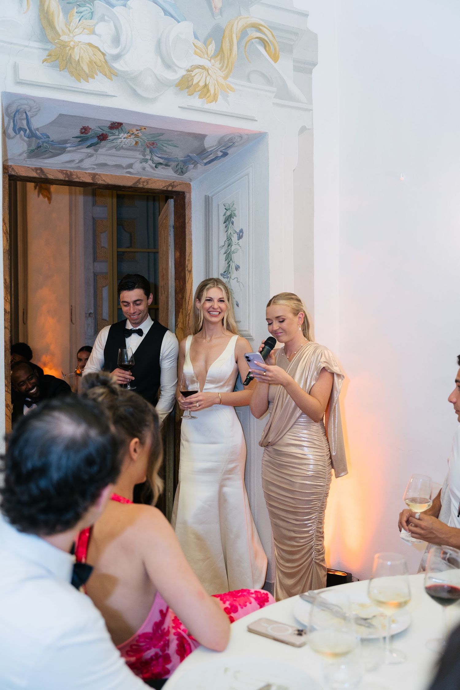 Bride and bridesmaid giving speech at elegant Italian castle wedding reception.