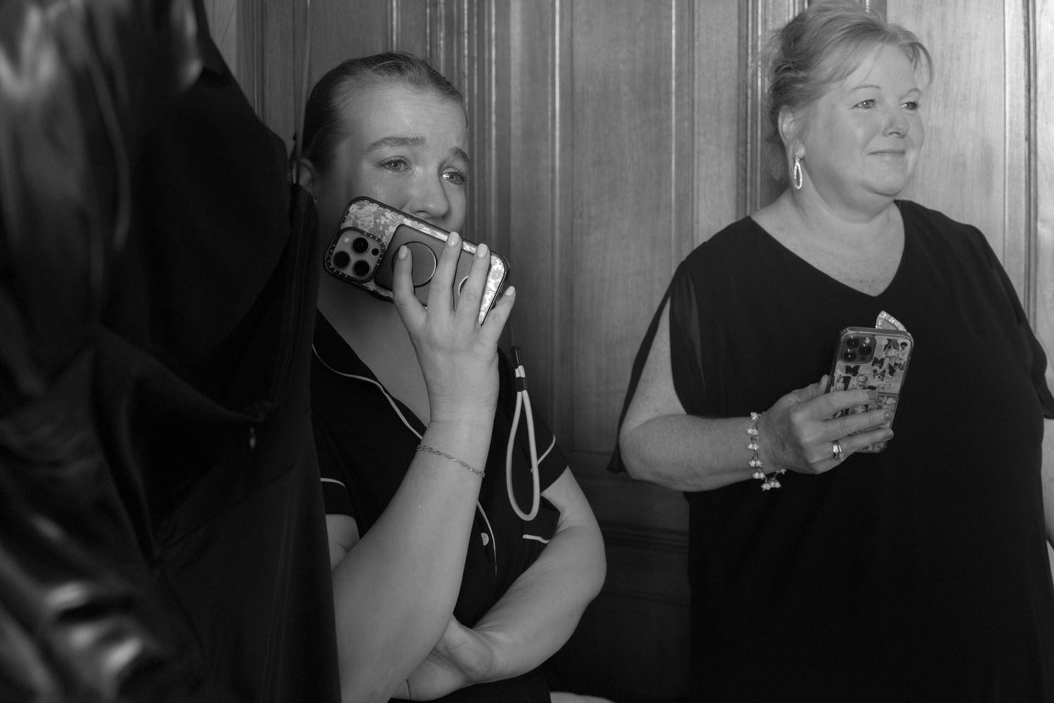 Black and white photo of two women capturing wedding moments on smartphones in elegant venue interior.